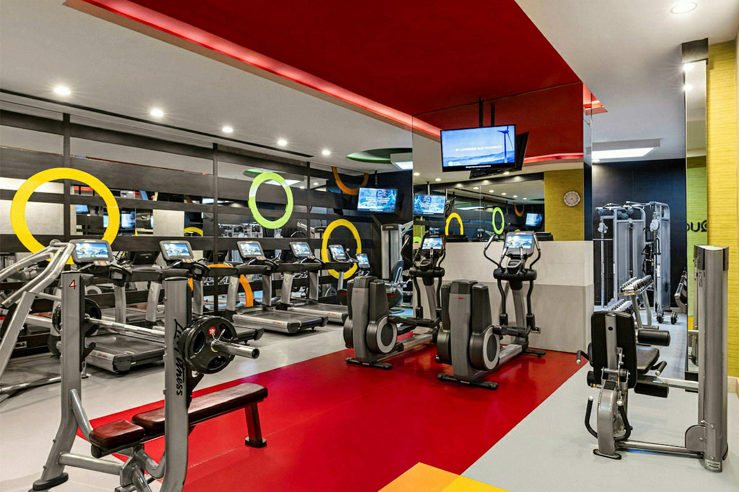 Et billede af et fitnesscenter med forskellige træningsapparater såsom løbebånd, crosstrainere og andre maskiner, samt farverigt interiør. (AI-genereret tekst)