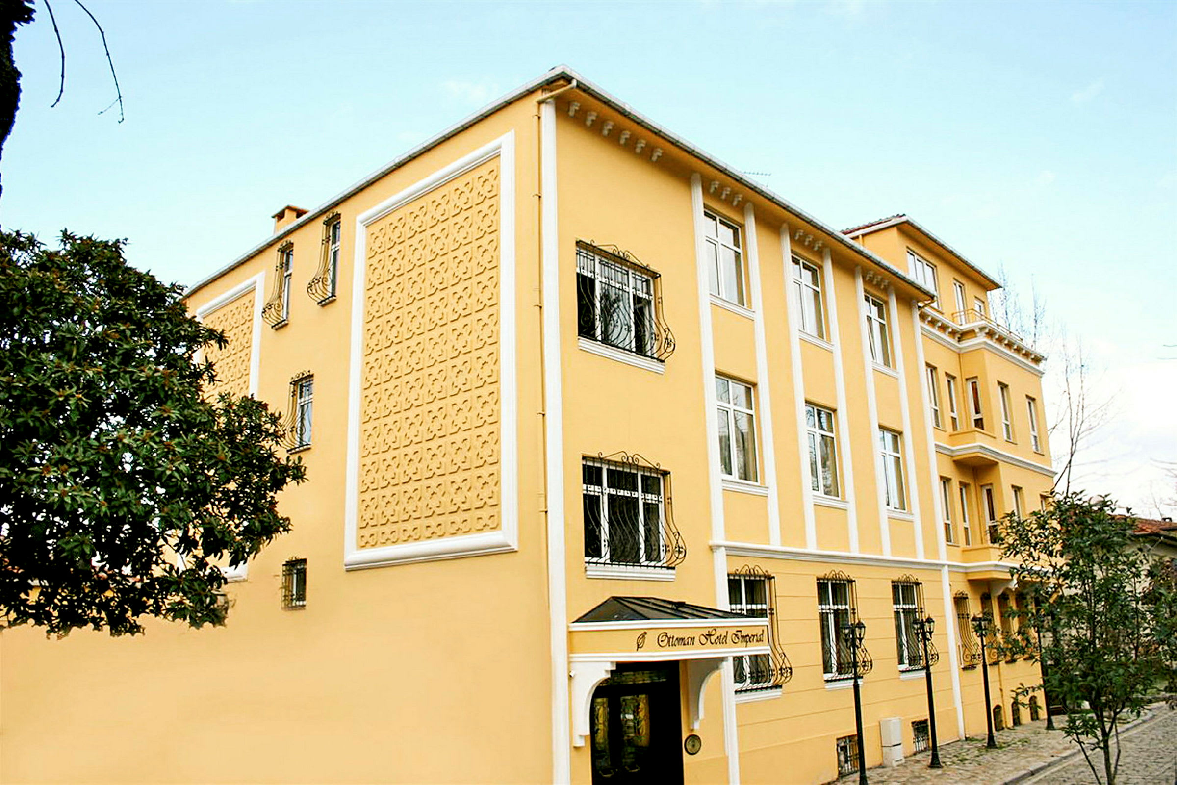 Et gult hotel med dekorativ facade, vinduer med jerngitre og en indgang med overdækning. (AI-genereret tekst)