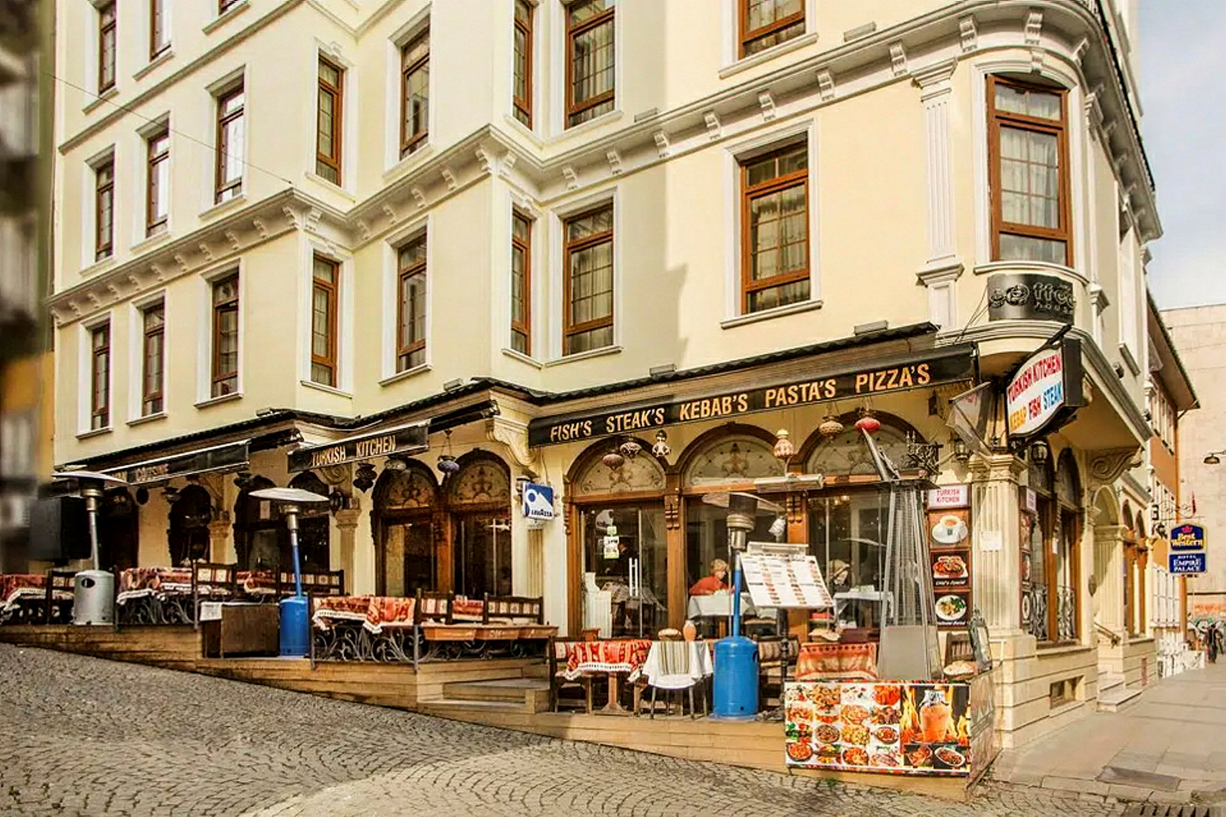 En gade med en bygning med restaurant og udendørs servering, skilte med mad som kebab og pizza. (AI-genereret tekst)