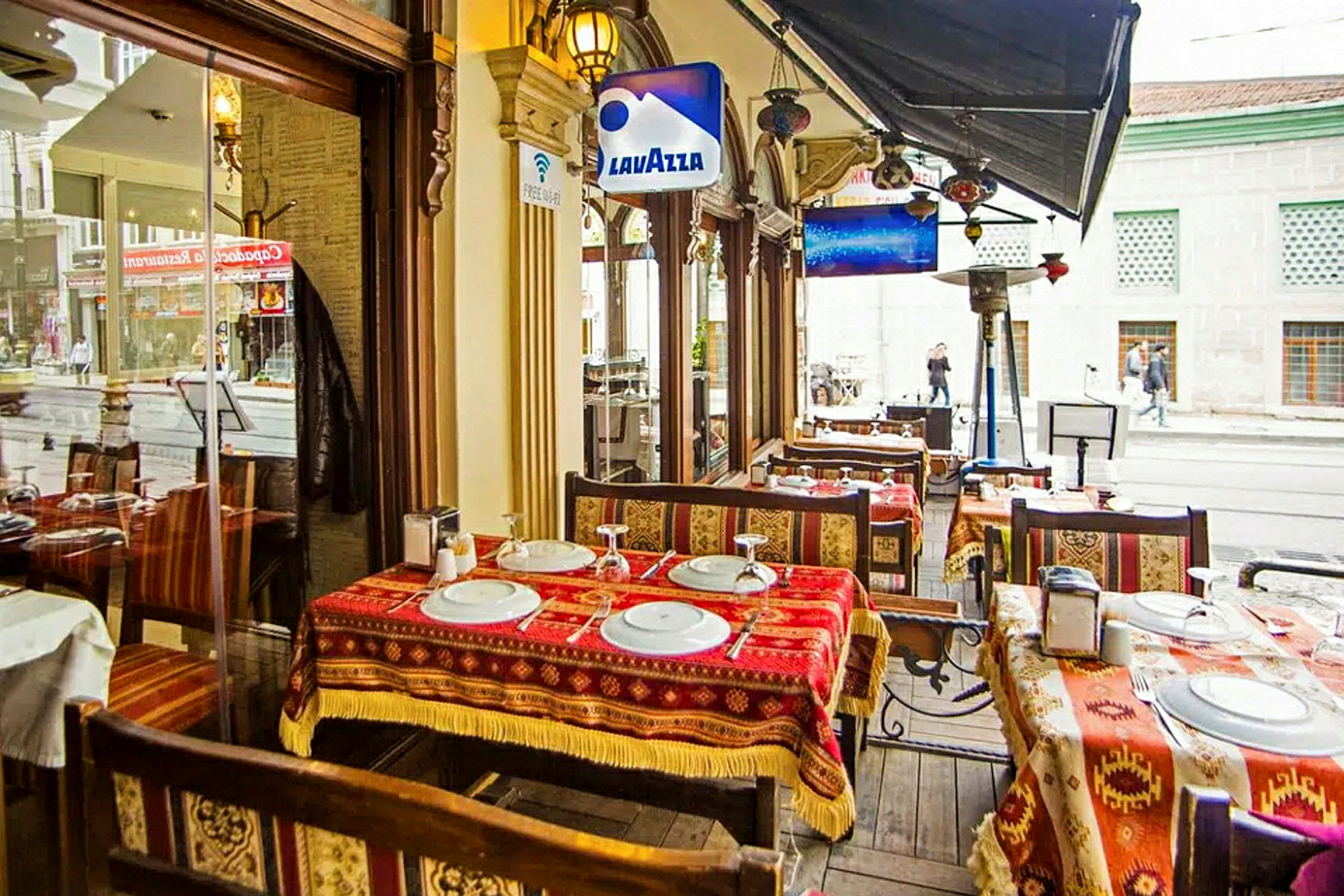 En udendørs servering ved en restaurant med borde, stole og mønstrede duge. (AI-genereret tekst)
