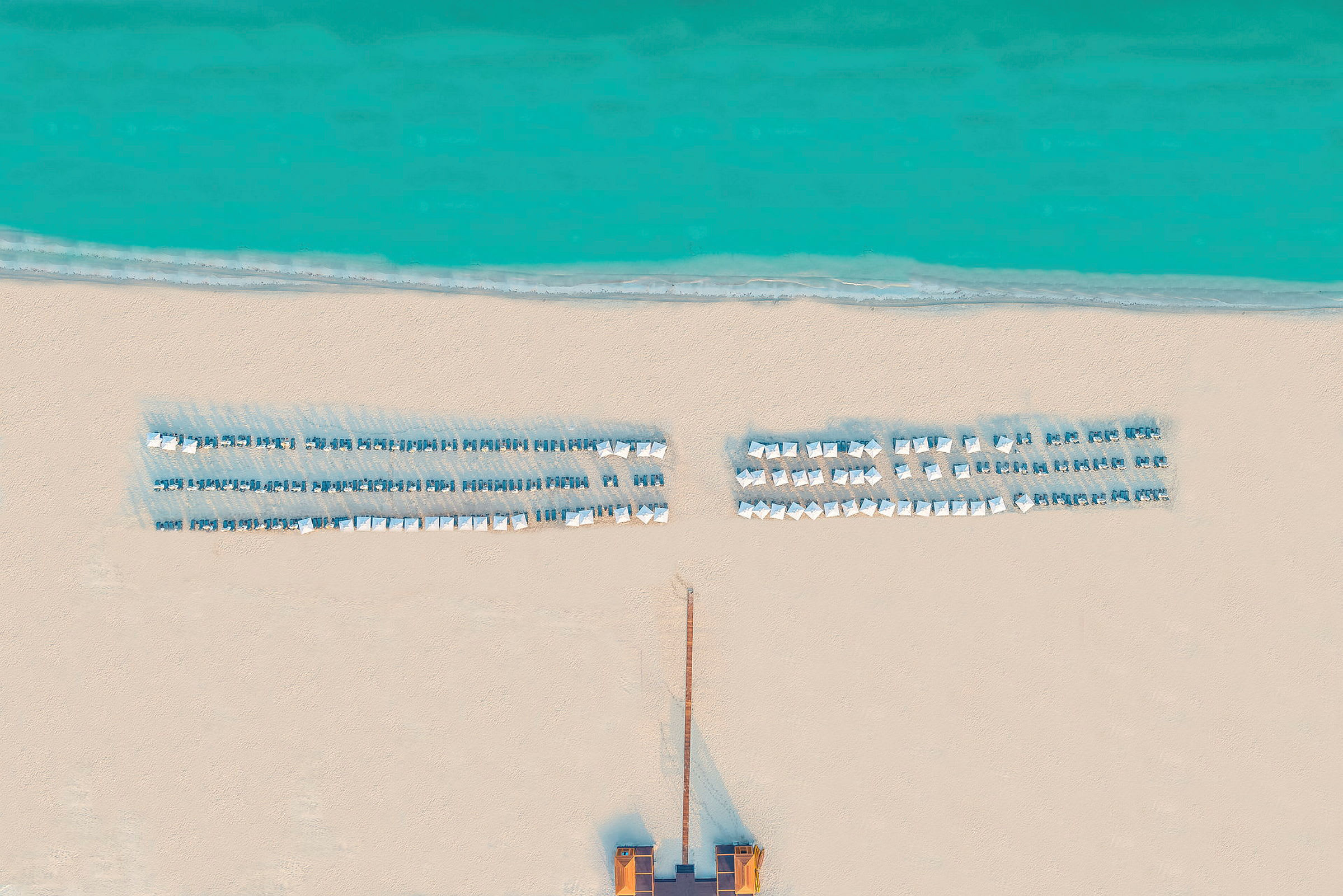 Luftfoto af en strand med liggestole og parasoller ved havet. (AI-genereret tekst)
