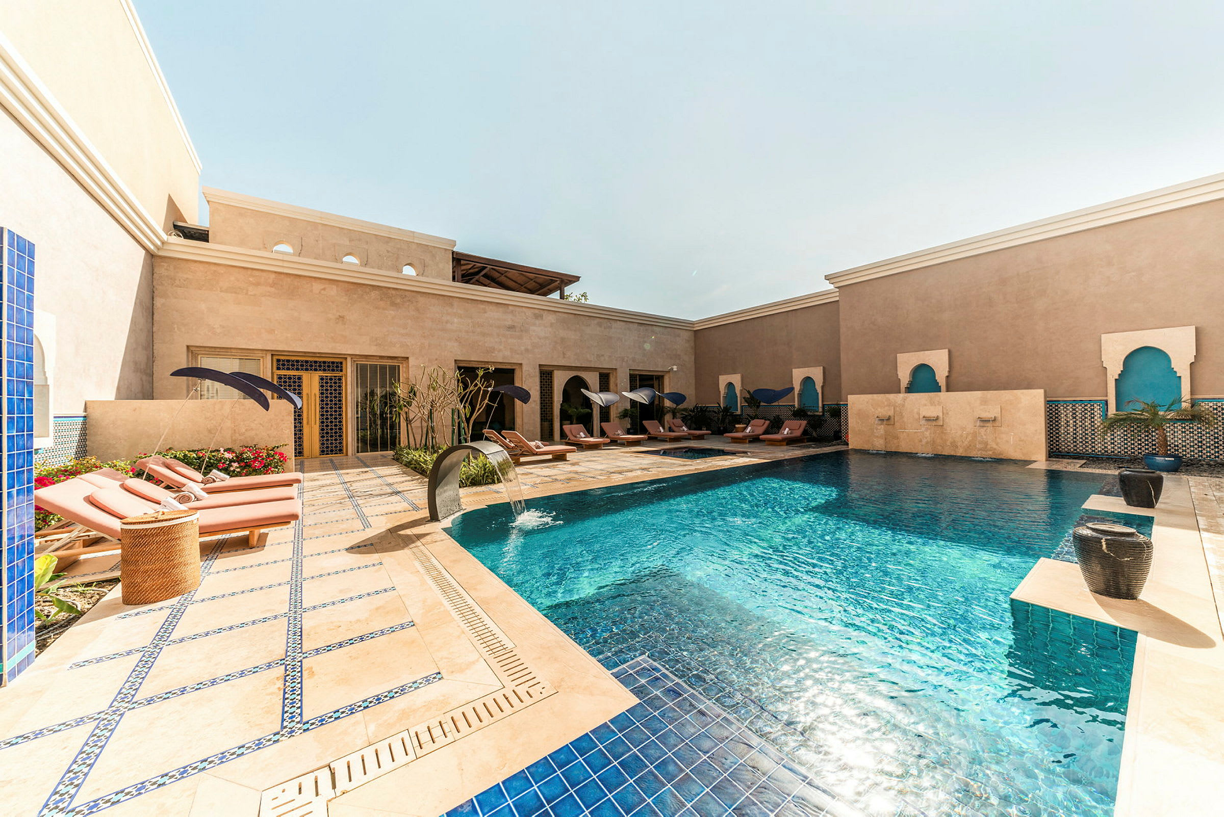 Billede af en udendørs pool omgivet af liggestole og parasoller ved et stilfuldt hotel. (AI-genereret tekst)