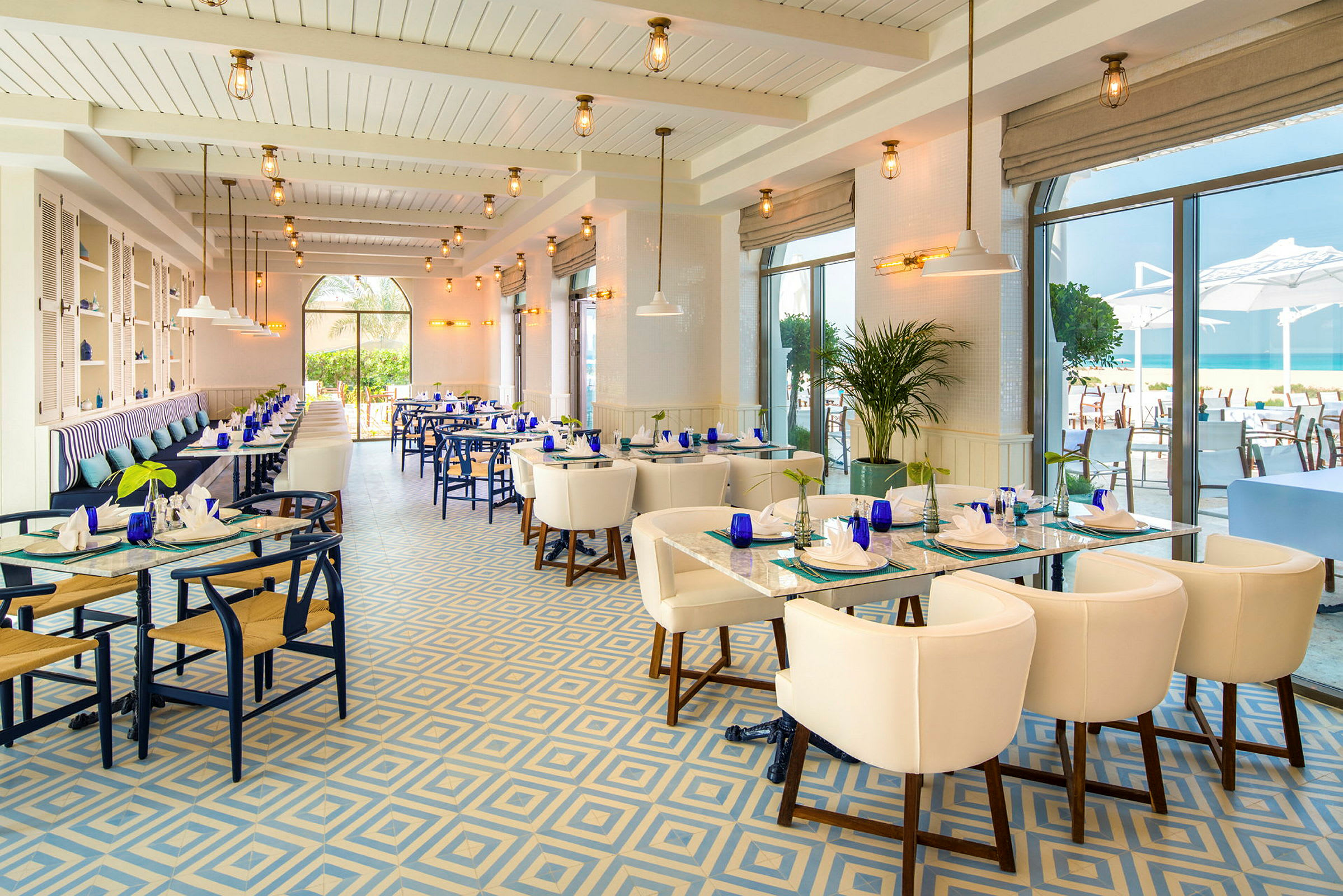 En elegant restaurant med store vinduer, blå og hvide farvetoner og udsigt til havet. (AI-genereret tekst)