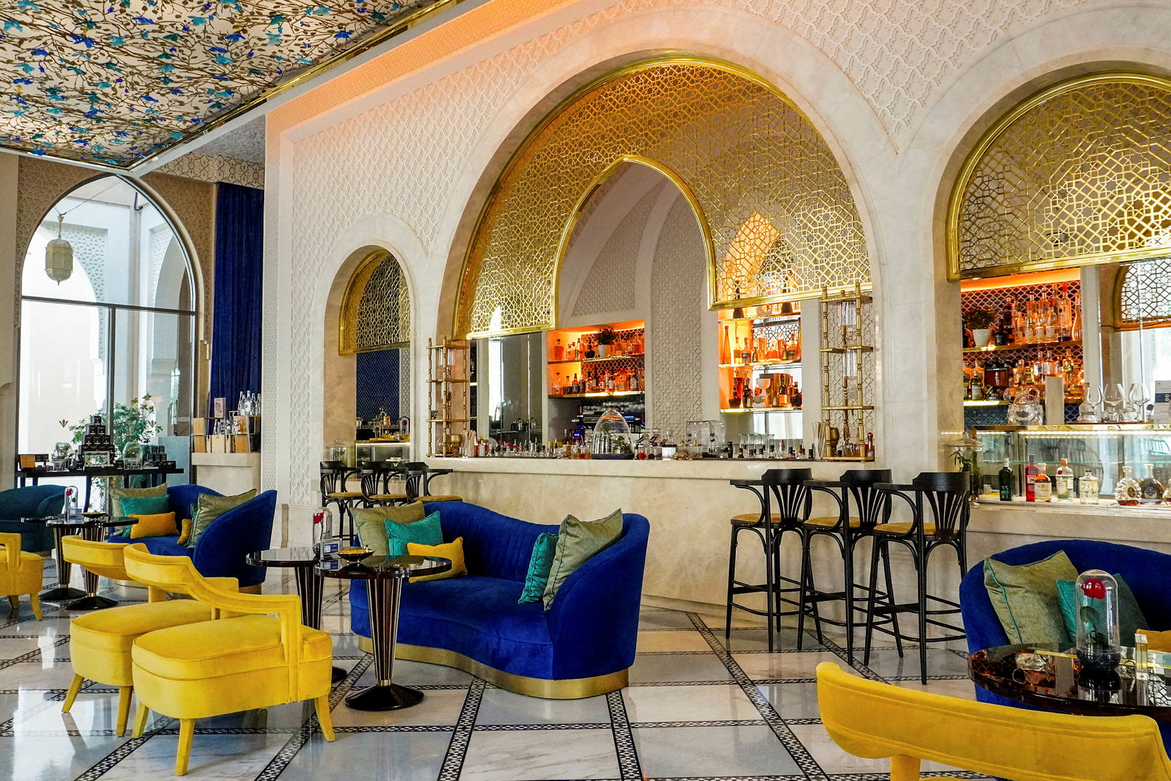 En elegant lounge med blå og gule møbler, et dekorativt loft og en bar med gyldne detaljer. (AI-genereret tekst)