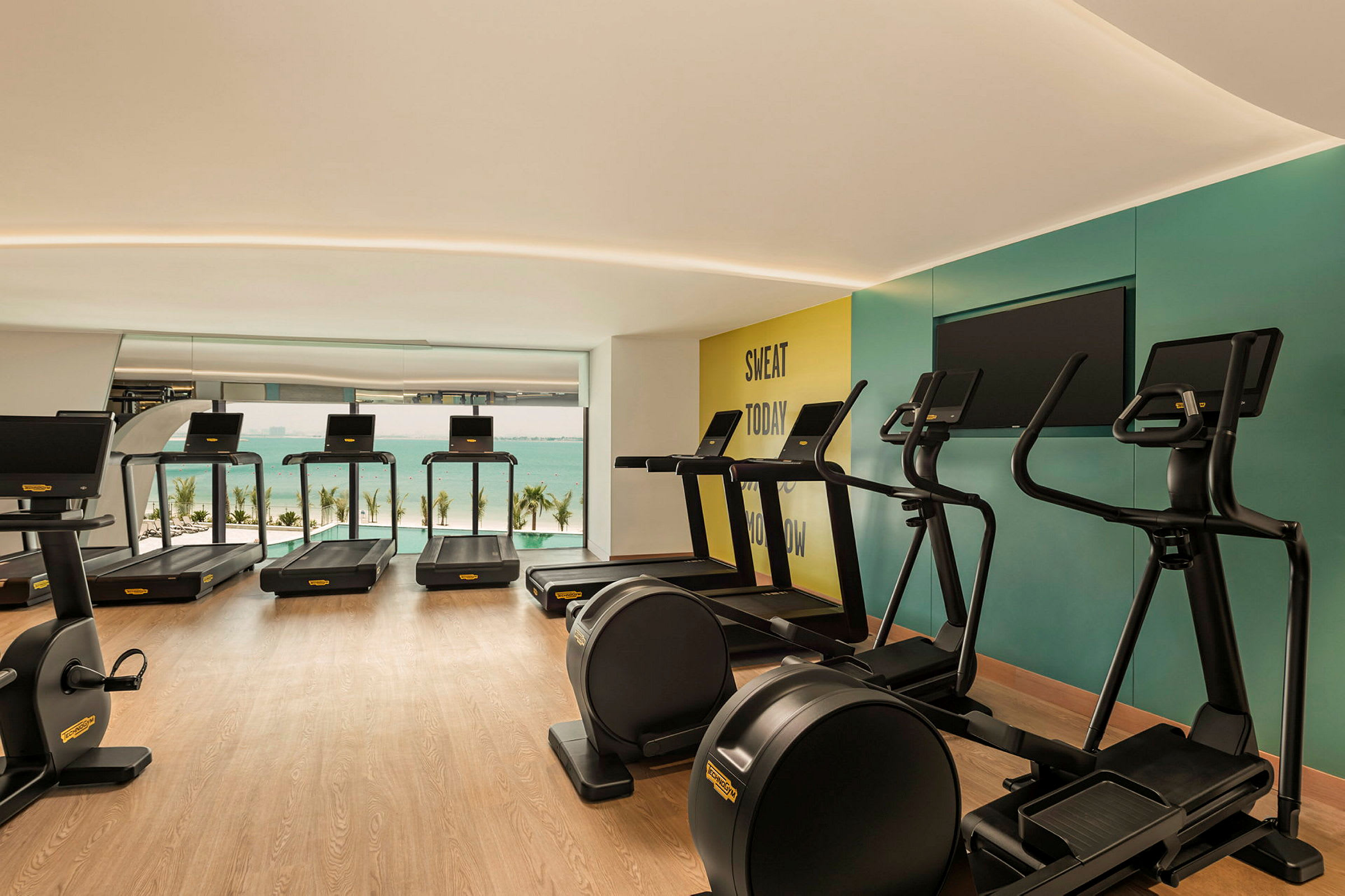 Et moderne fitnesscenter med løbebånd, motionscykler og udsigt over havet. (AI-genereret tekst)