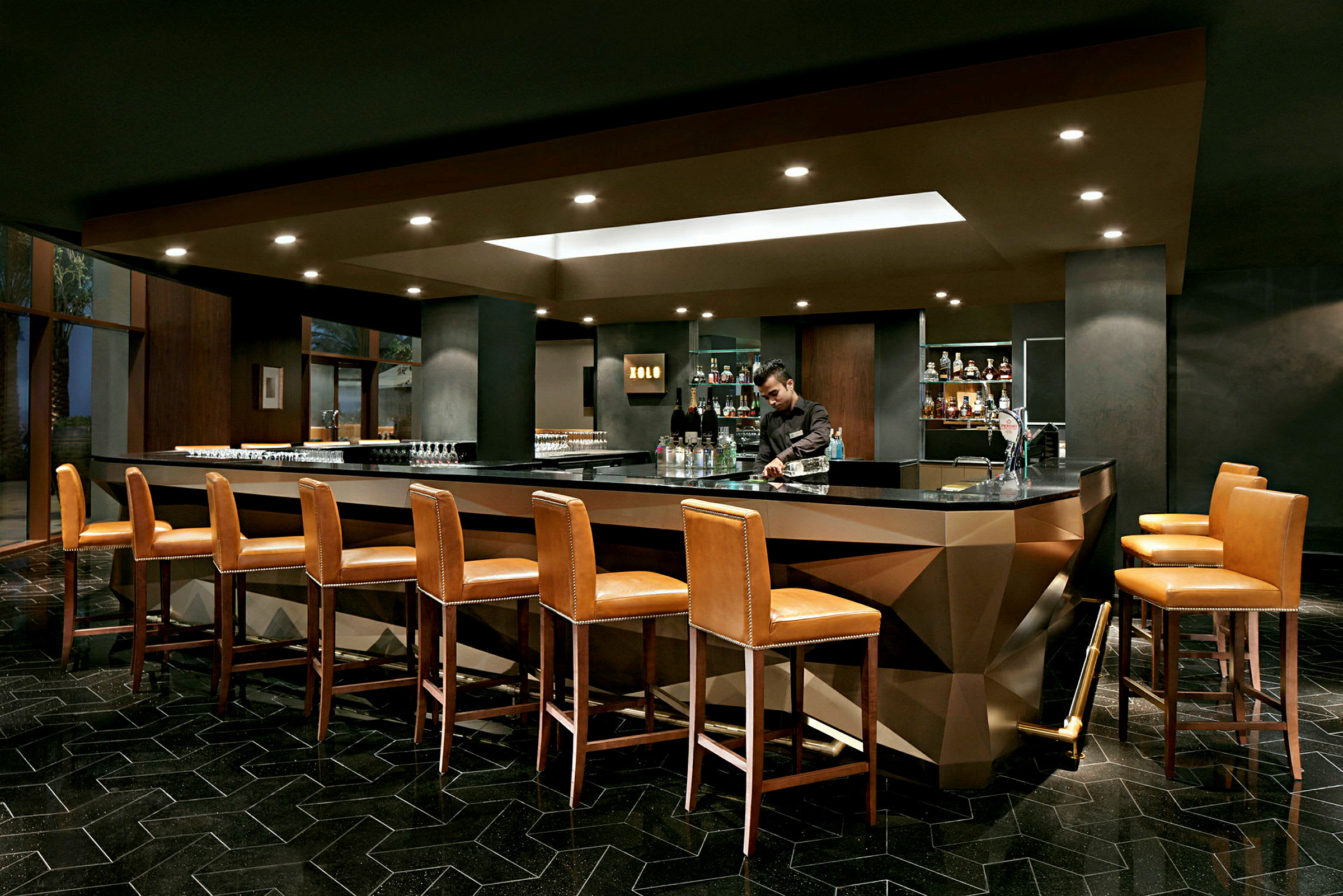 En elegant bar med høje læderstole placeret omkring en moderne bardisk i et stilfuldt interiør. (AI-genereret tekst)
