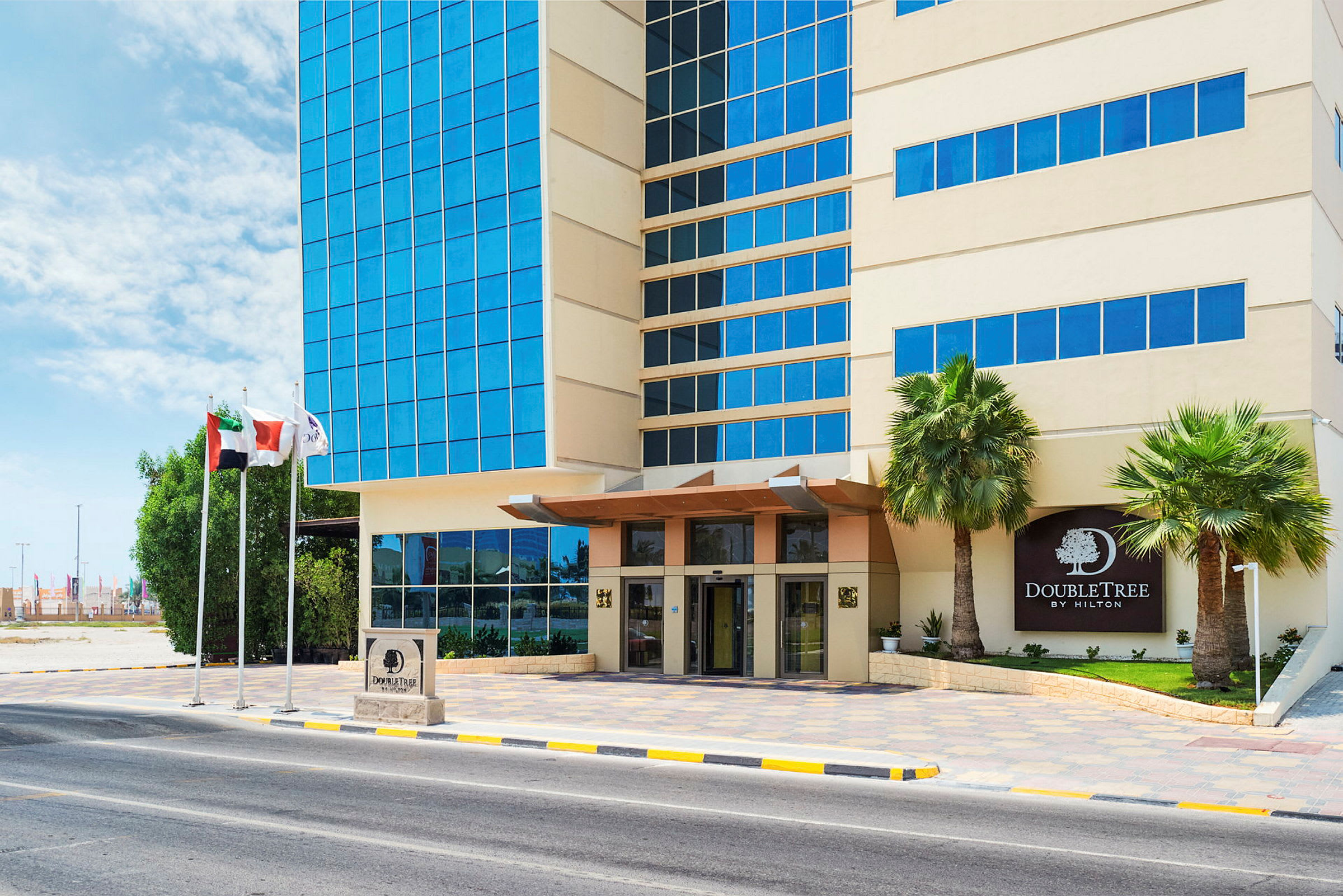 Eksteriør af DoubleTree Hotel med indgang, glasfacade og palmer ved siden af. (AI-genereret tekst)