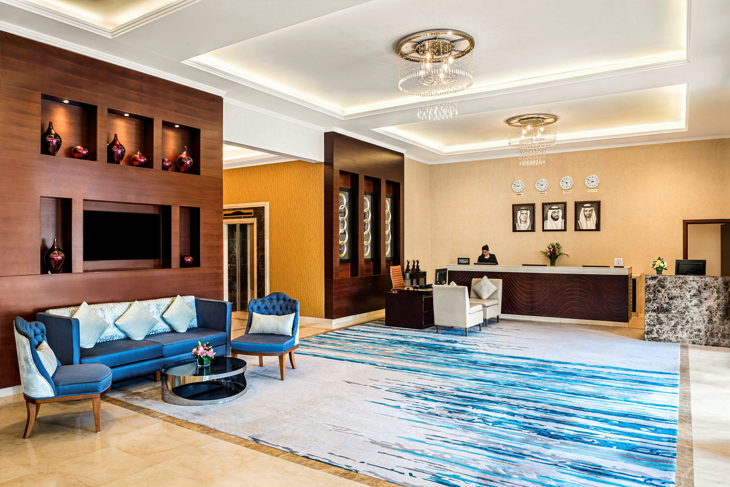En elegant hotelreception med en siddegruppe med blå sofaer, et dekorativt receptionsområde og et marmorgulv. (AI-genereret tekst)