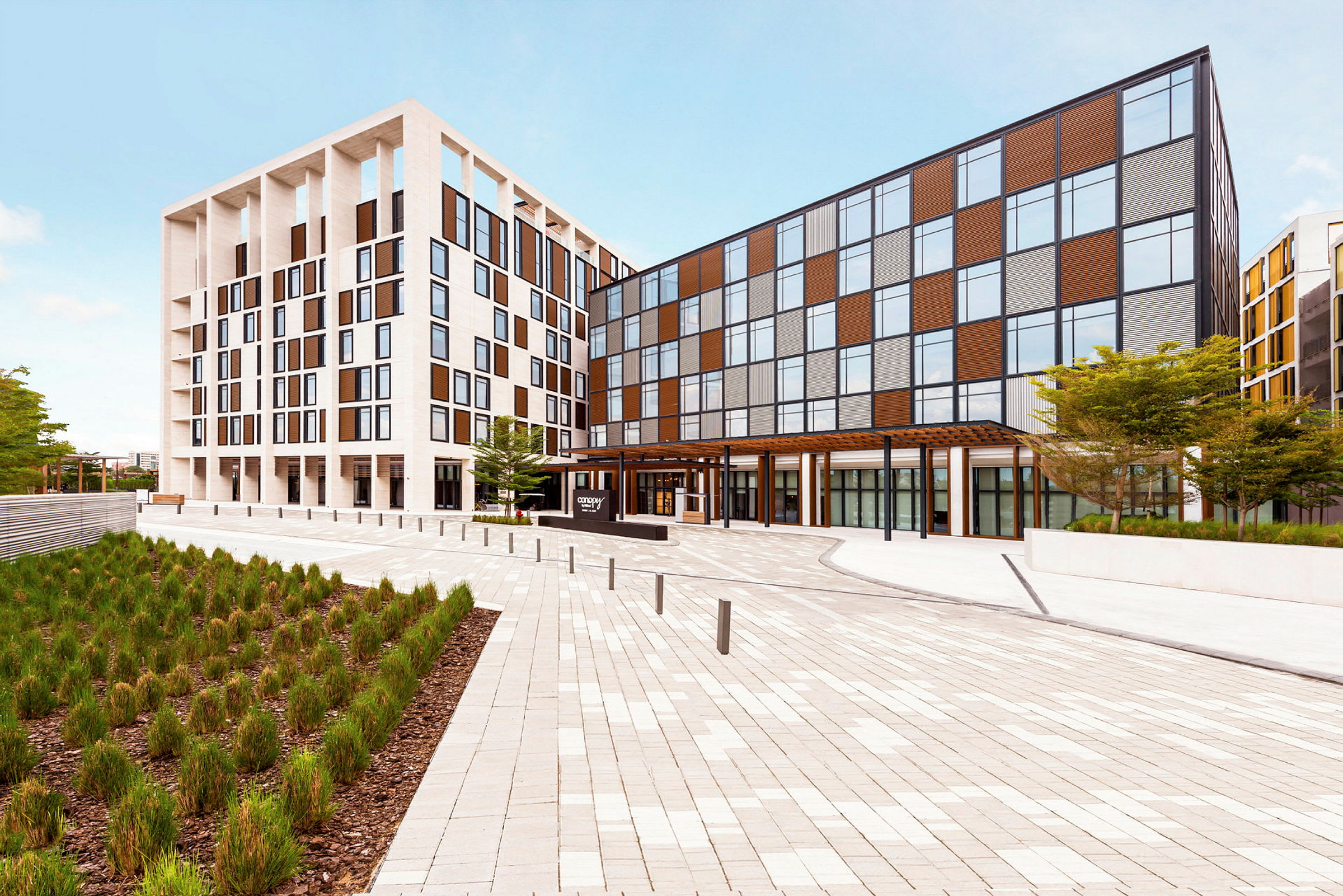 Et moderne hotel med en lys facade og store vinduer, beliggende ved en åben plads. (AI-genereret tekst)