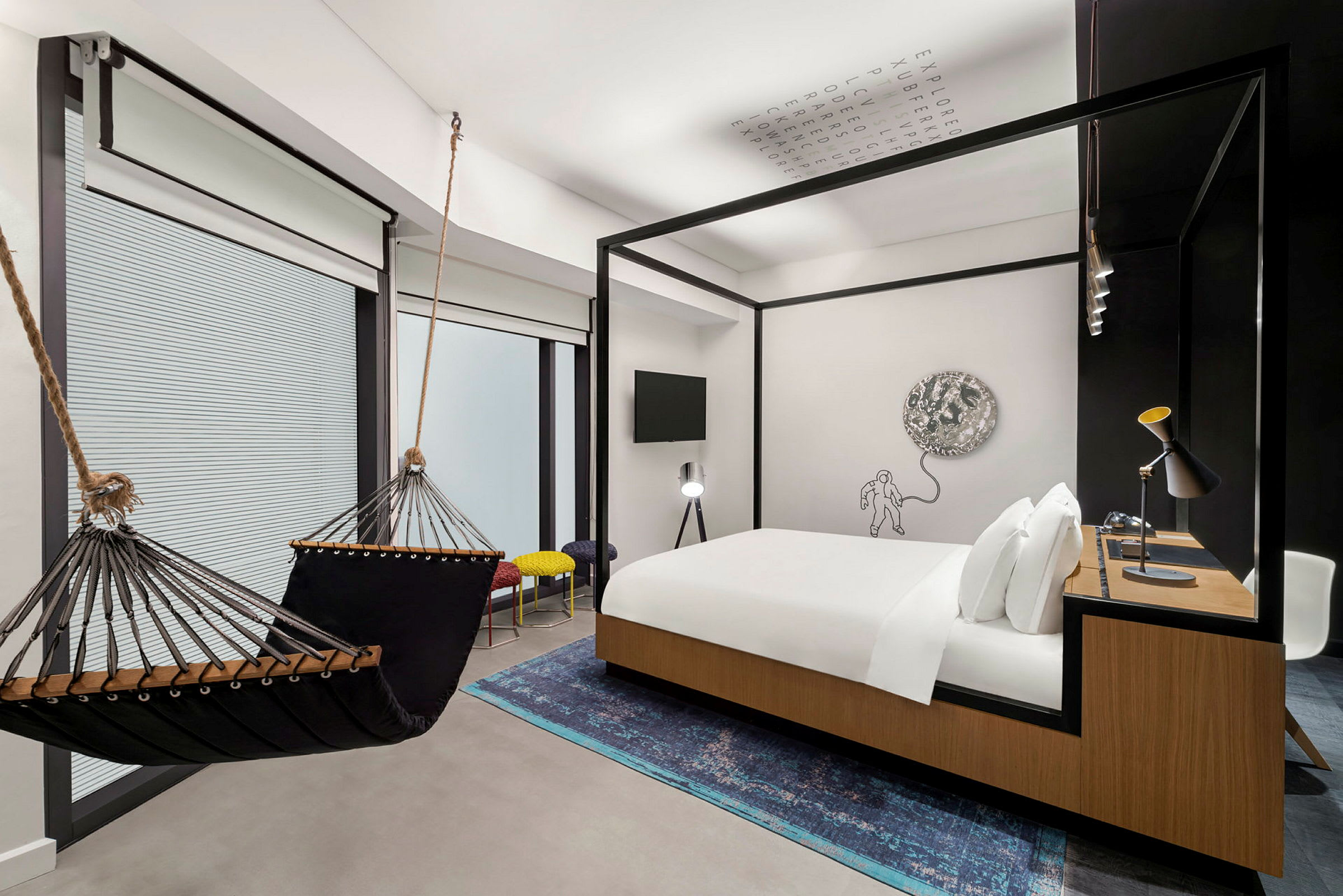 Et moderne hotelværelse med en hængekøje, en dobbeltseng med trædetaljer, et skrivebord og en kunstnerisk vægdekoration. (AI-genereret tekst)