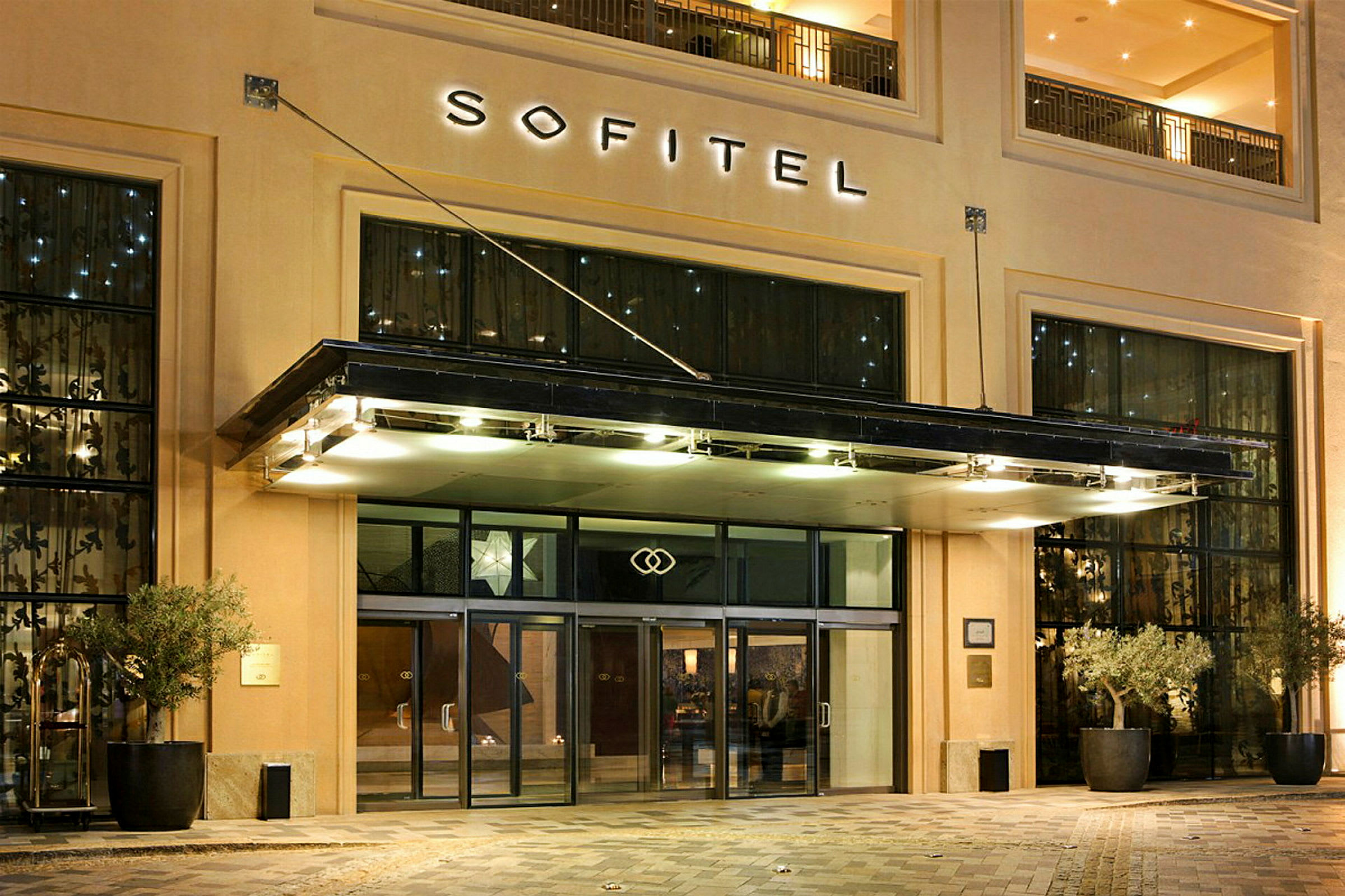Indgangen til hotel Sofitel med glasdøre og belysning. (AI-genereret tekst)