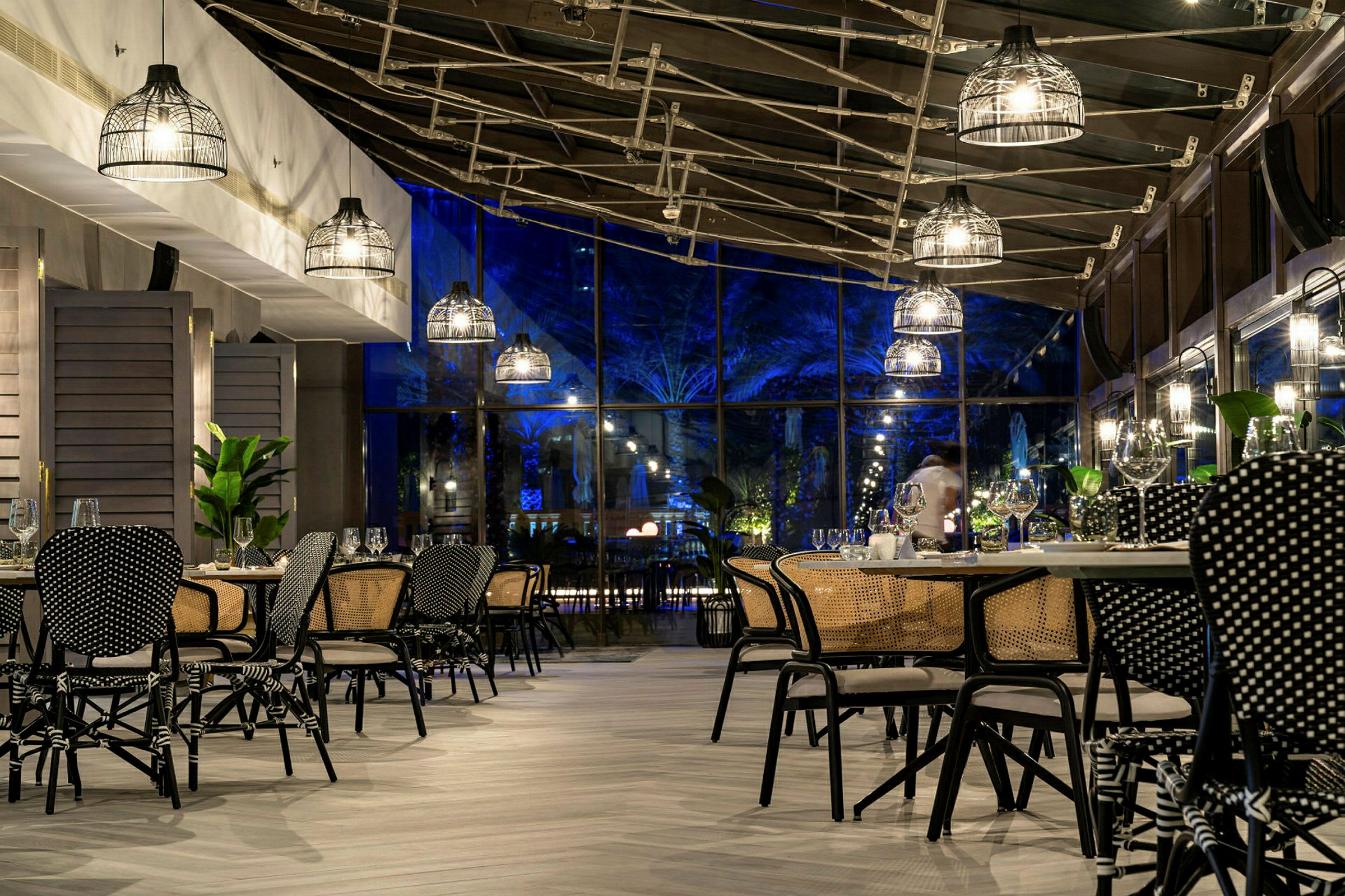 En restaurant med moderne møbler og loftslamper samt glasvægge, der viser udendørs belysning om aftenen. (AI-genereret tekst)
