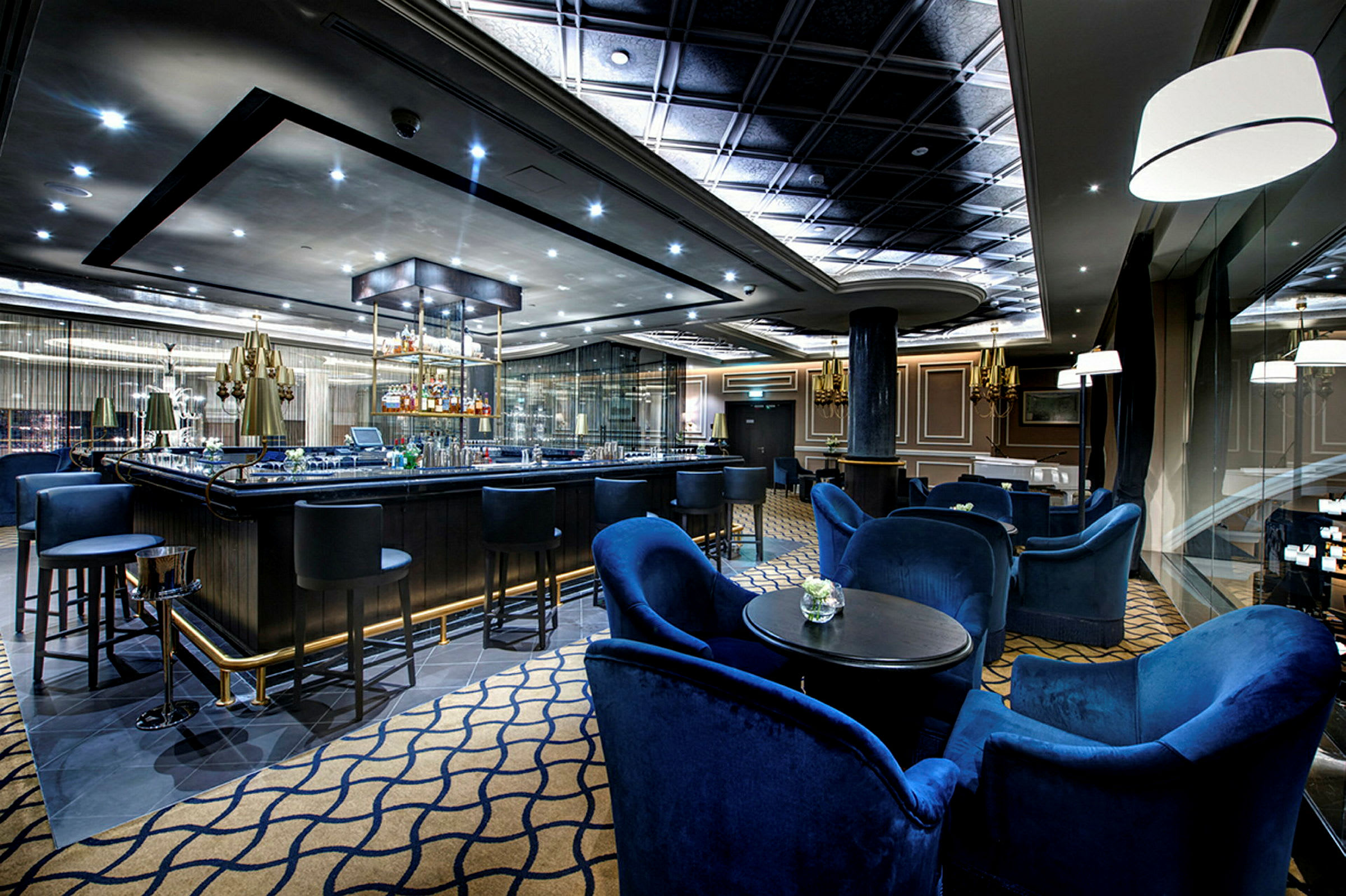 En elegant bar med blå stole og borde, oplyst loft samt glasdetaljer. (AI-genereret tekst)