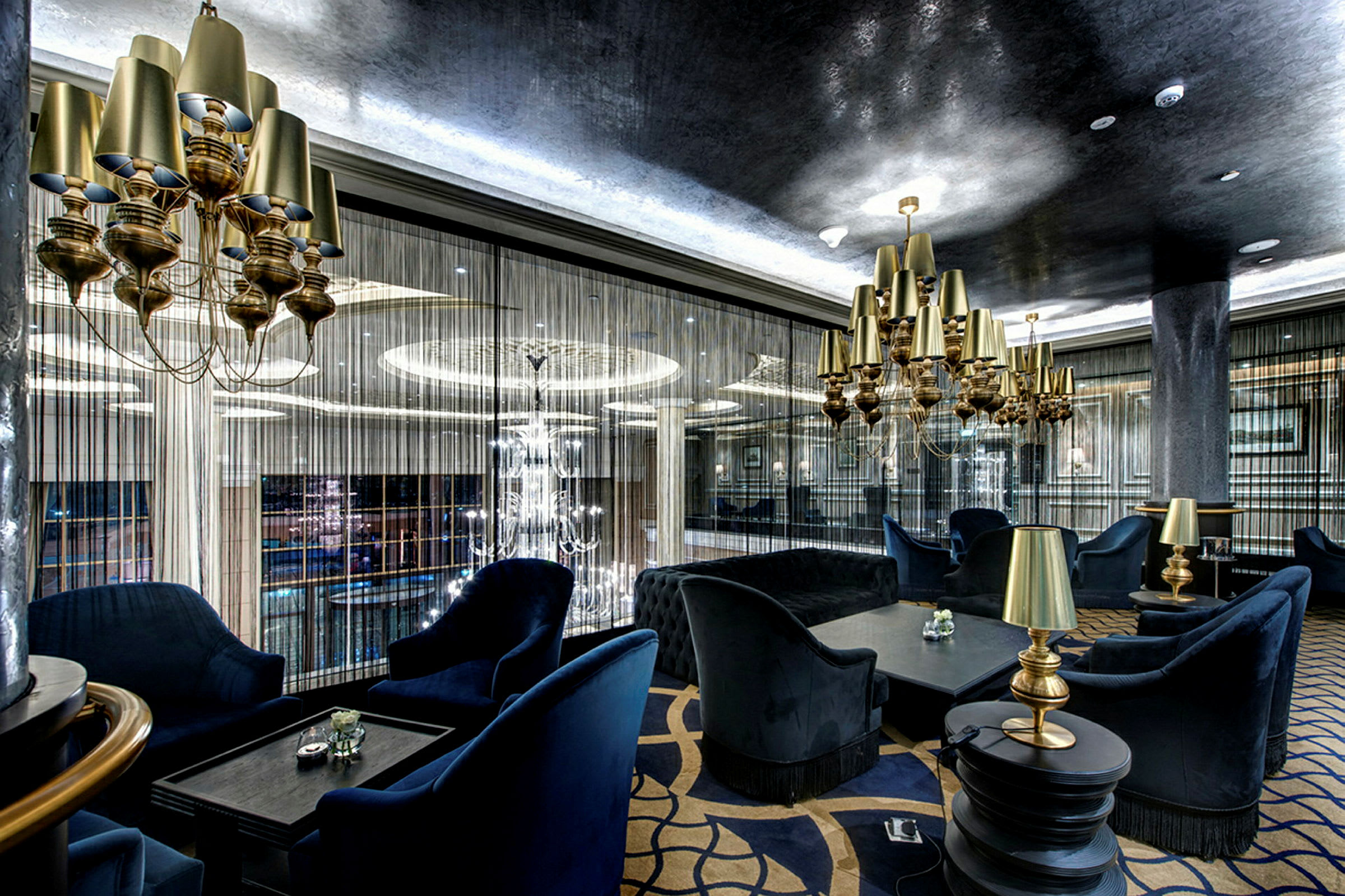 En elegant lounge med blå polstrede møbler, guldlamper og moderne hængende lysekroner. (AI-genereret tekst)