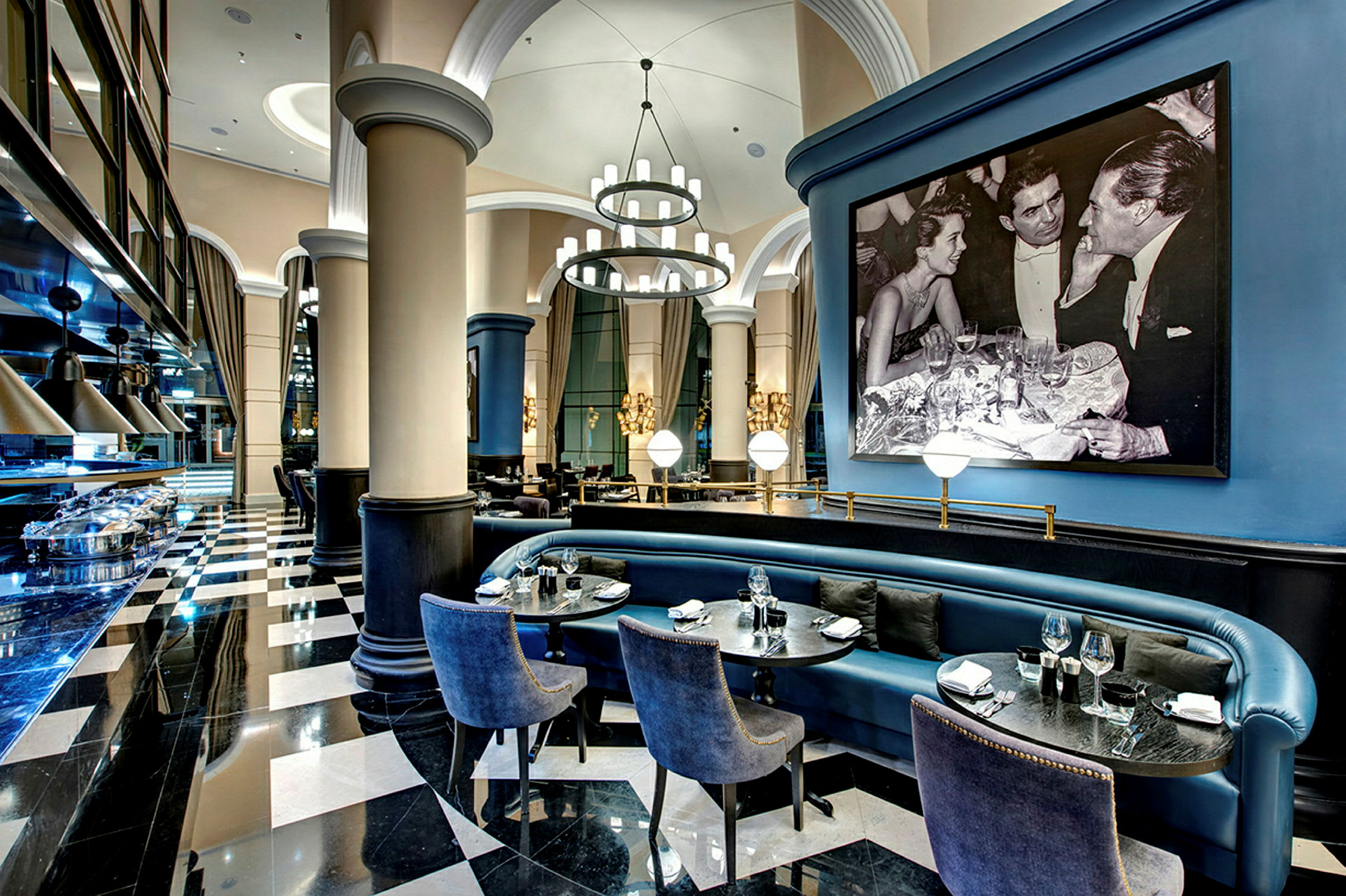 Interiør af en elegant restaurant med sort-hvidt gulv, blå siddepladser og et stort indrammet sort-hvidt billede. (AI-genereret tekst)