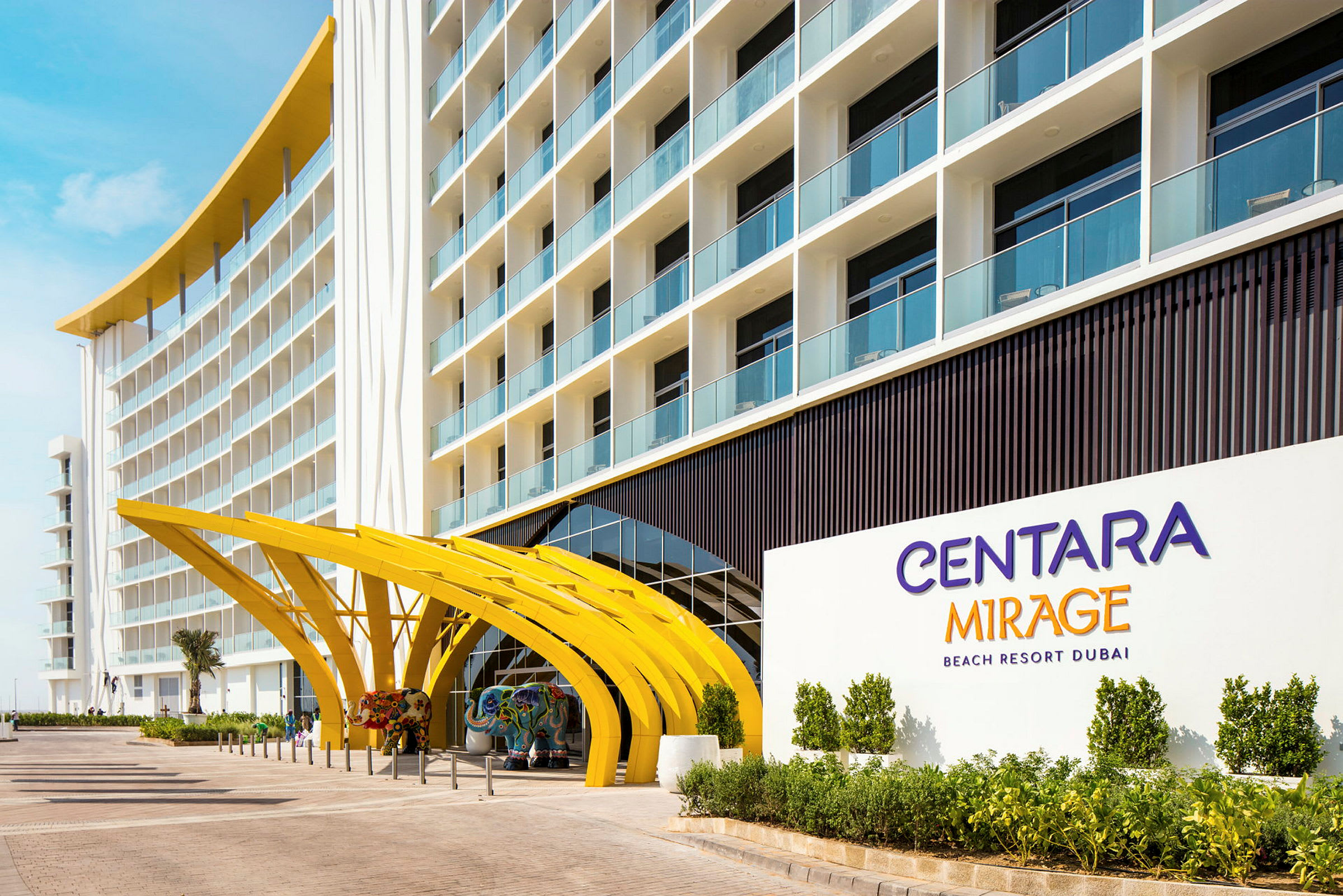 Indgangen til et hotel med buede gule strukturer og et skilt, der angiver "Centara Mirage Beach Resort Dubai". (AI-genereret tekst)