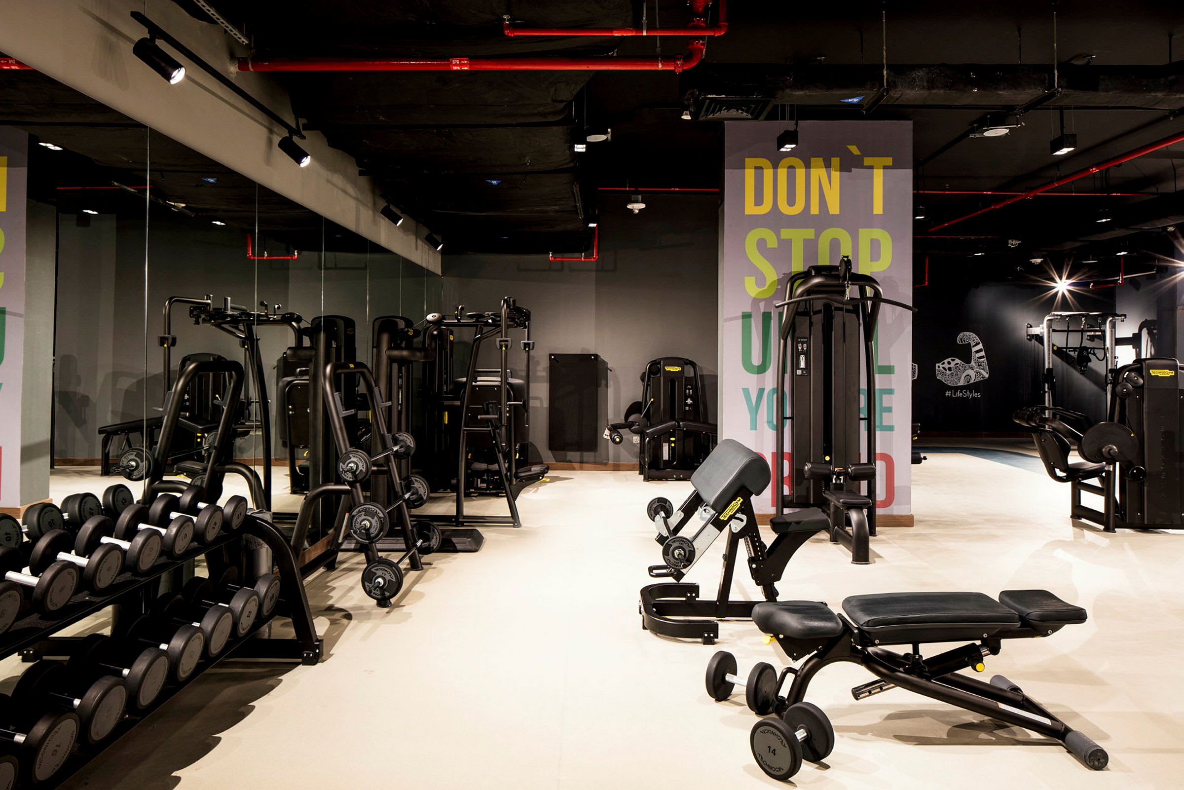 Et fitnesscenter med forskellige træningsmaskiner og håndvægte på et stativ, med en spejlvæg i baggrunden. (AI-genereret tekst)