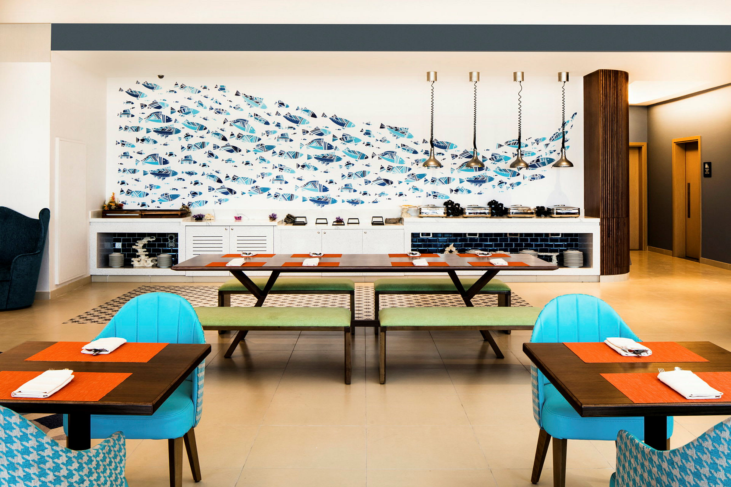 En restaurant med et moderne indrettet spiseområde, der inkluderer borde med farverige dækkeservietter, stole og en væg med fiskemotiv. (AI-genereret tekst)