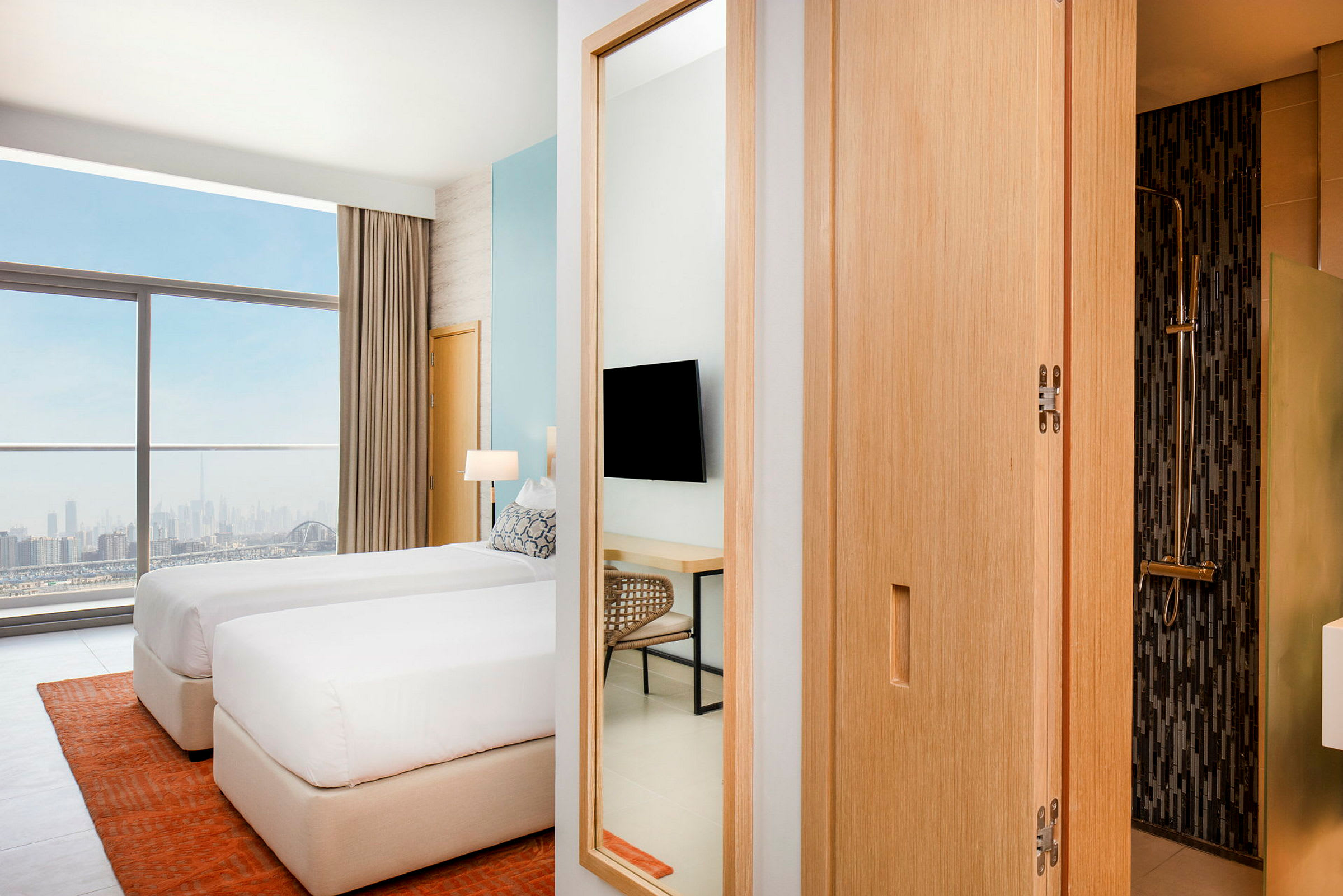 Et moderne hotelværelse med to enkeltsenge placeret nær et stort vindue med udsigt over en bysilhuet. Et badeværelse er delvis synligt til højre. (AI-genereret tekst)