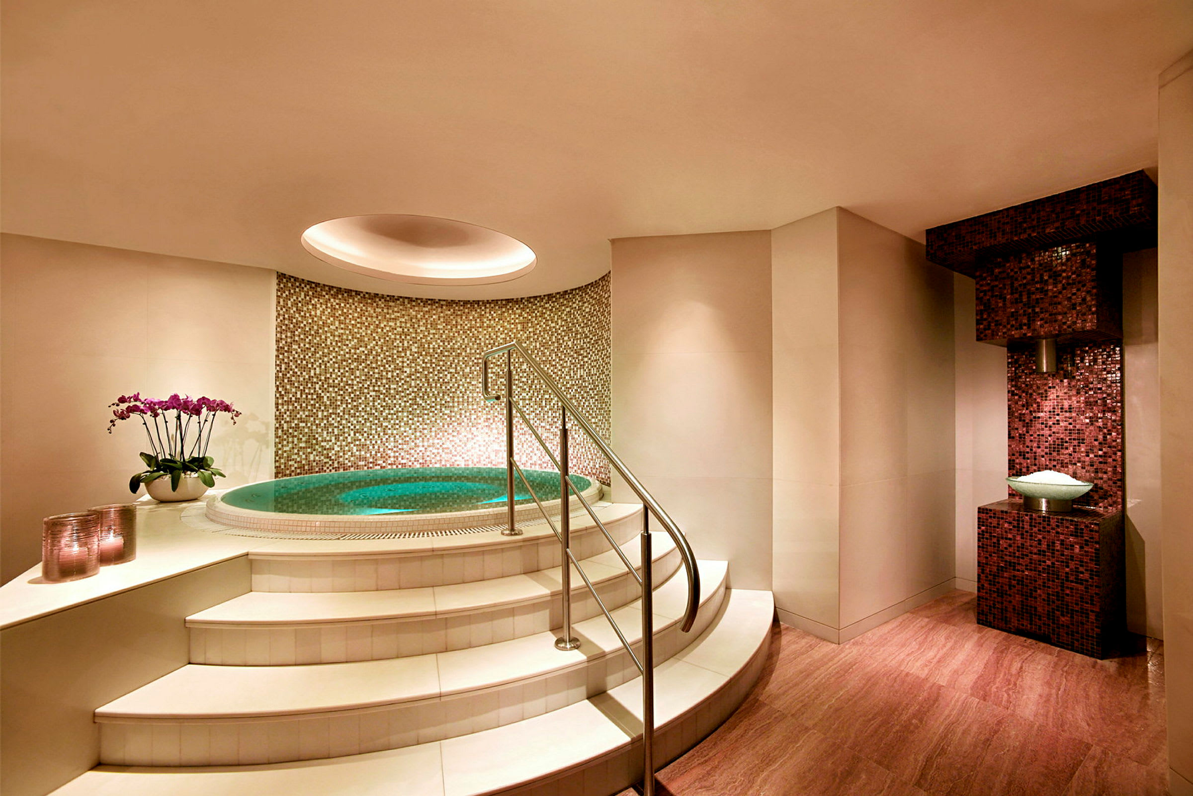 Billede af et lille spaområde med jacuzzi, trapper og mosaikvæg. (AI-genereret tekst)