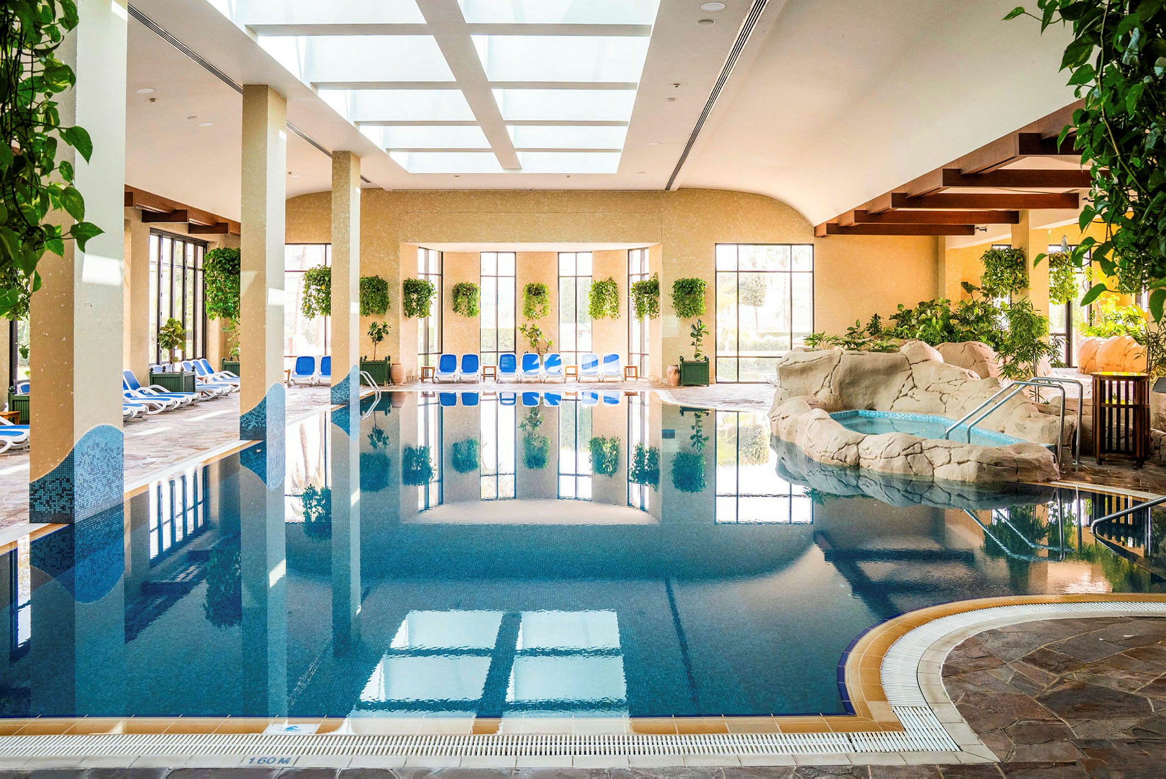 Indendørs swimmingpool med solvogne og grønne planter omkring. (AI-genereret tekst)
