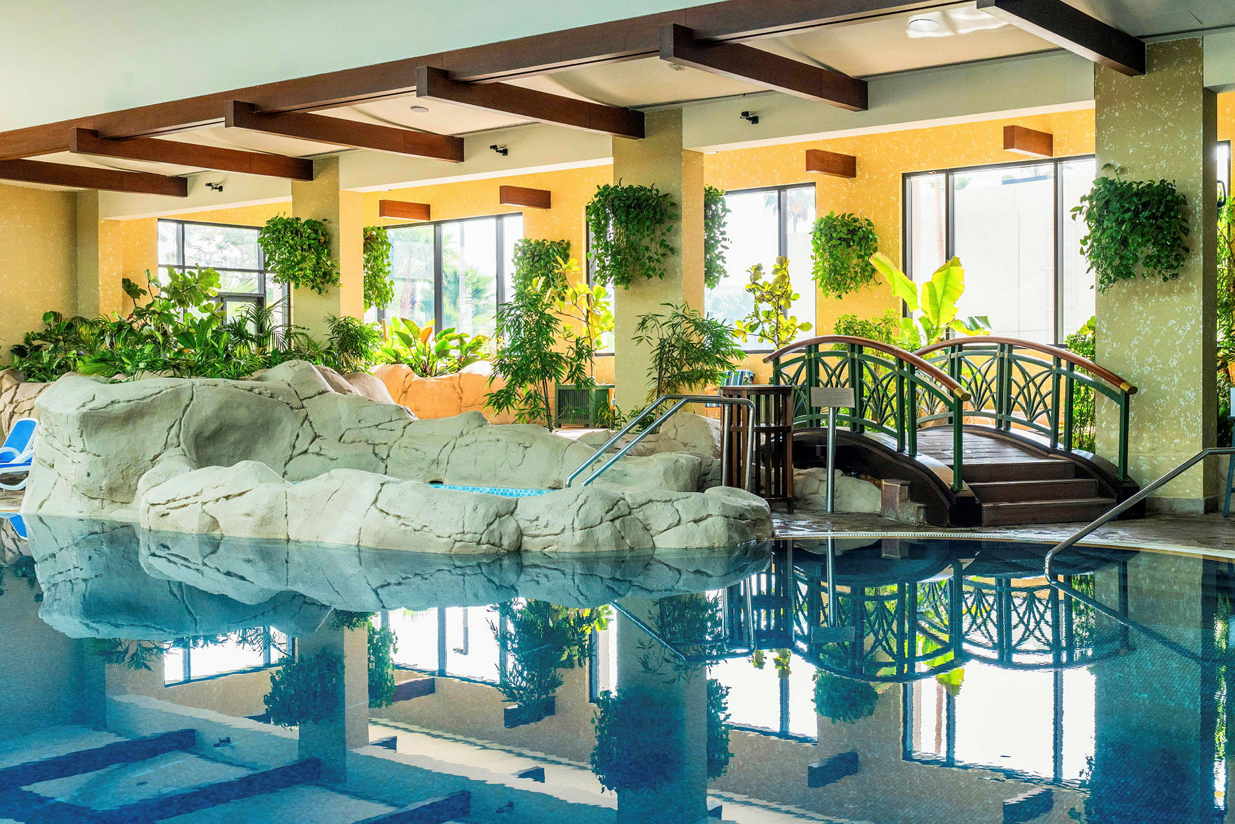 Billede af en indendørs pool med naturskøn dekoration, herunder planter og en lille bro. (AI-genereret tekst)