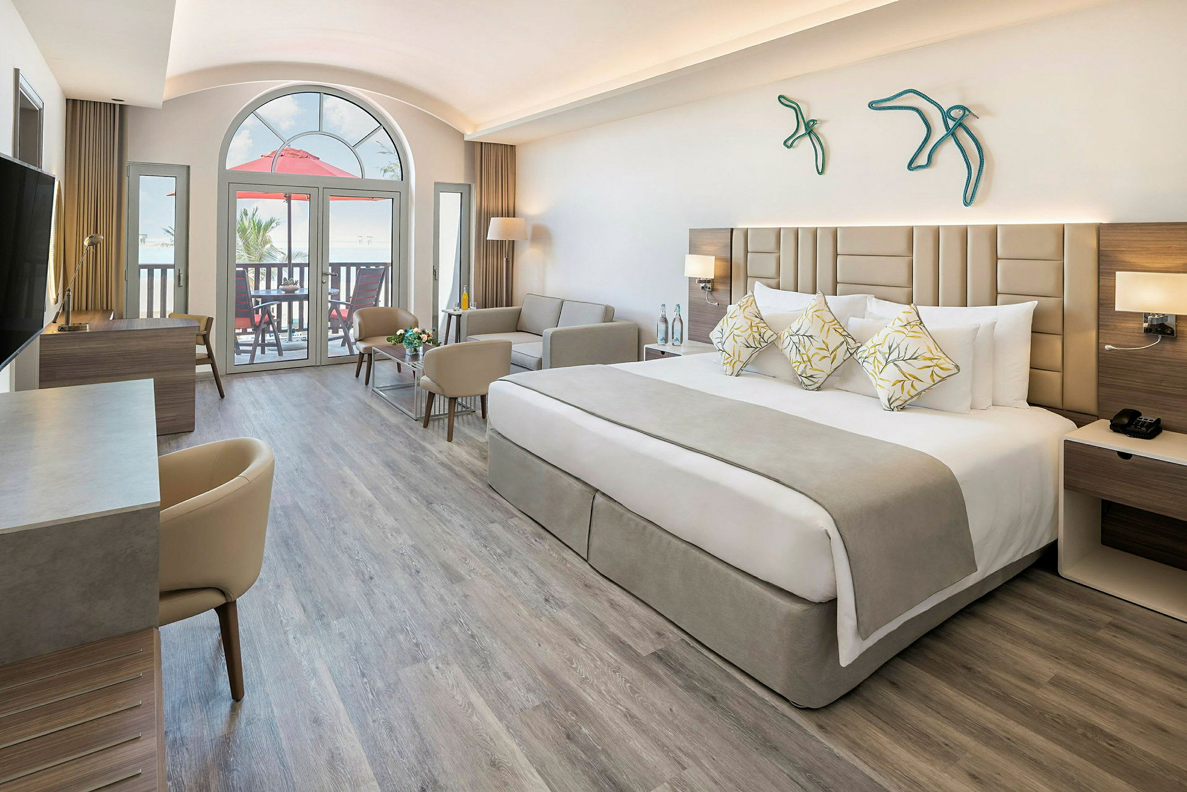 Et moderne hotelværelse med en bred seng, sofa og skrivebord. Store vinduer og balkon i baggrunden. (AI-genereret tekst)