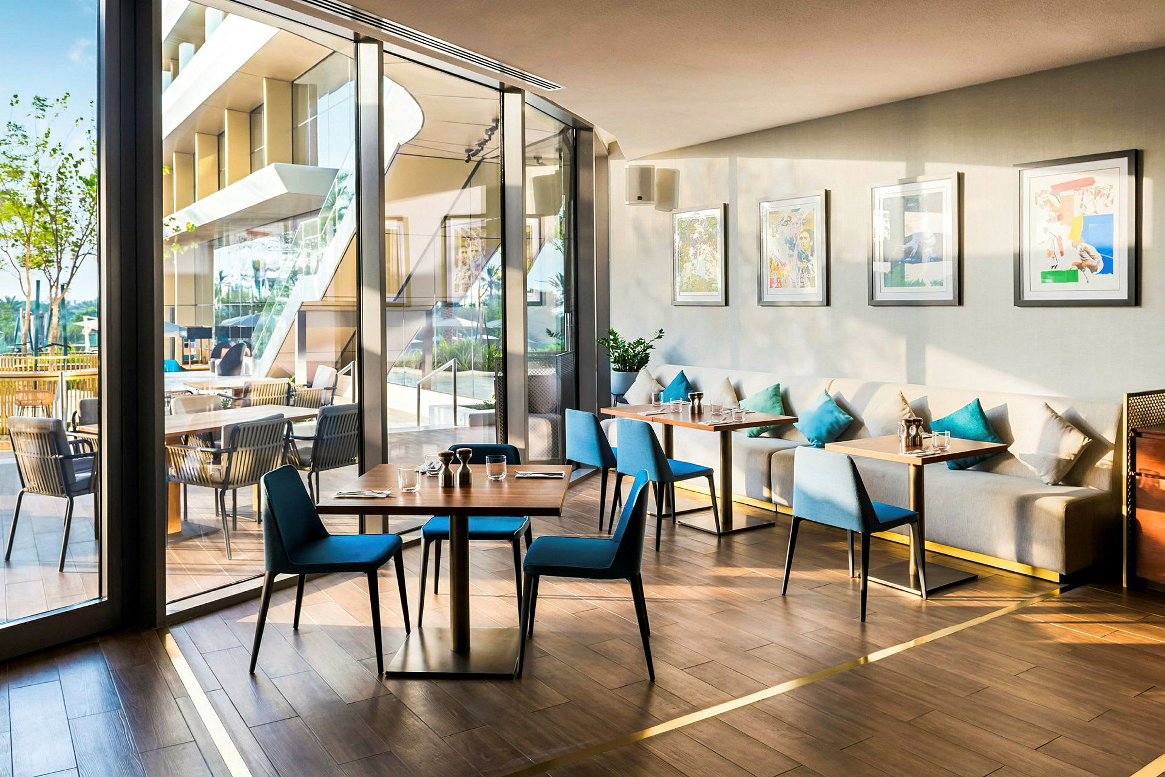 En lys og moderne restaurant med glasvægge, blå stole og sofaer med dekorative puder. (AI-genereret tekst)