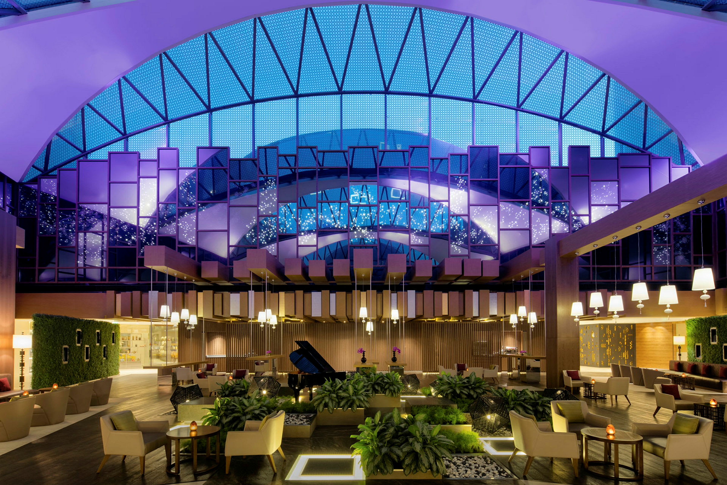 En elegant hotellobby med moderne møbler, planteudsmykning og store vinduer med glødende belysning. (AI-genereret tekst)