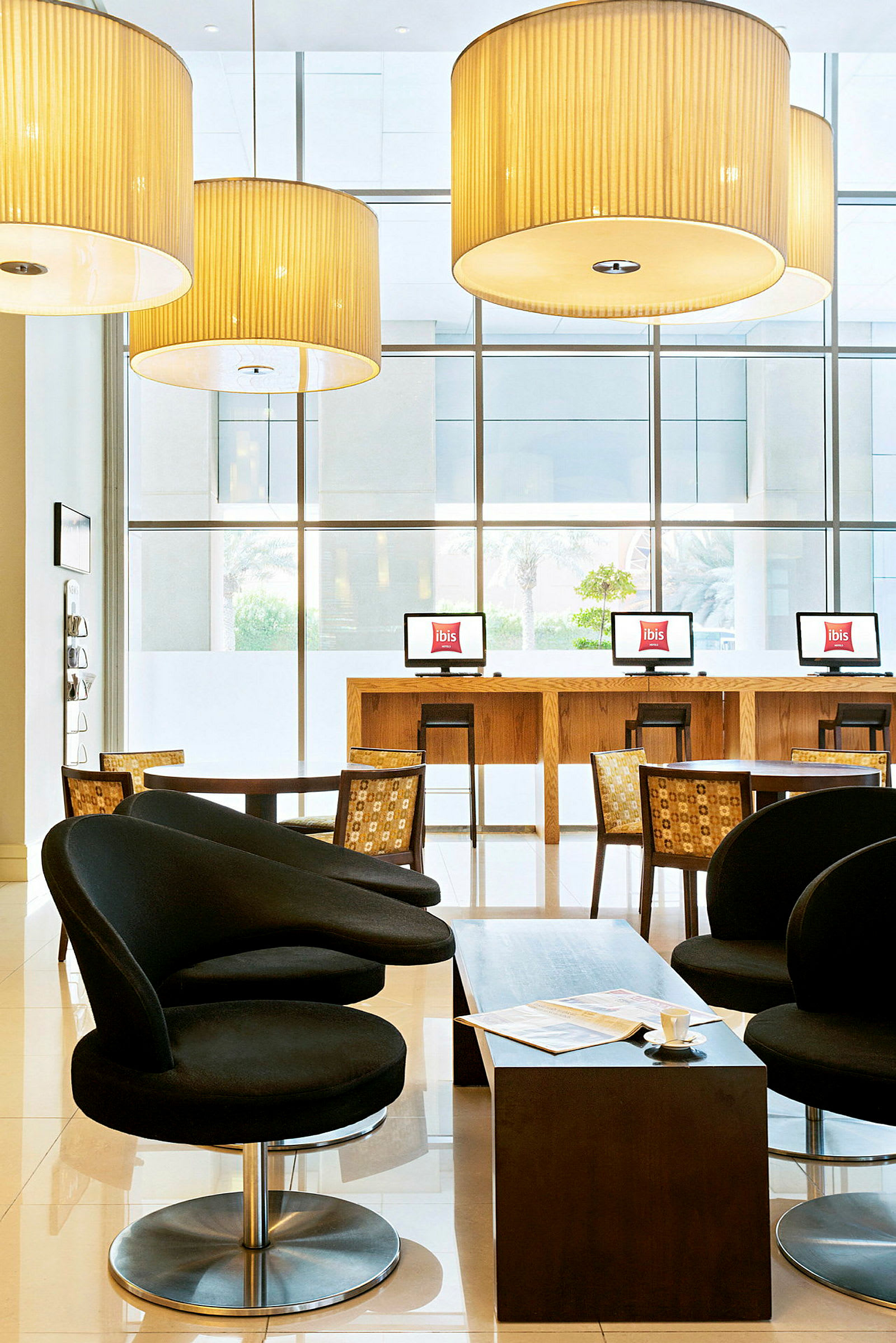 Et hotellets lobbyområde med sorte lænestole, et lavt bord og computere på en bardiskslignende skranke foran store vinduer. (AI-genereret tekst)