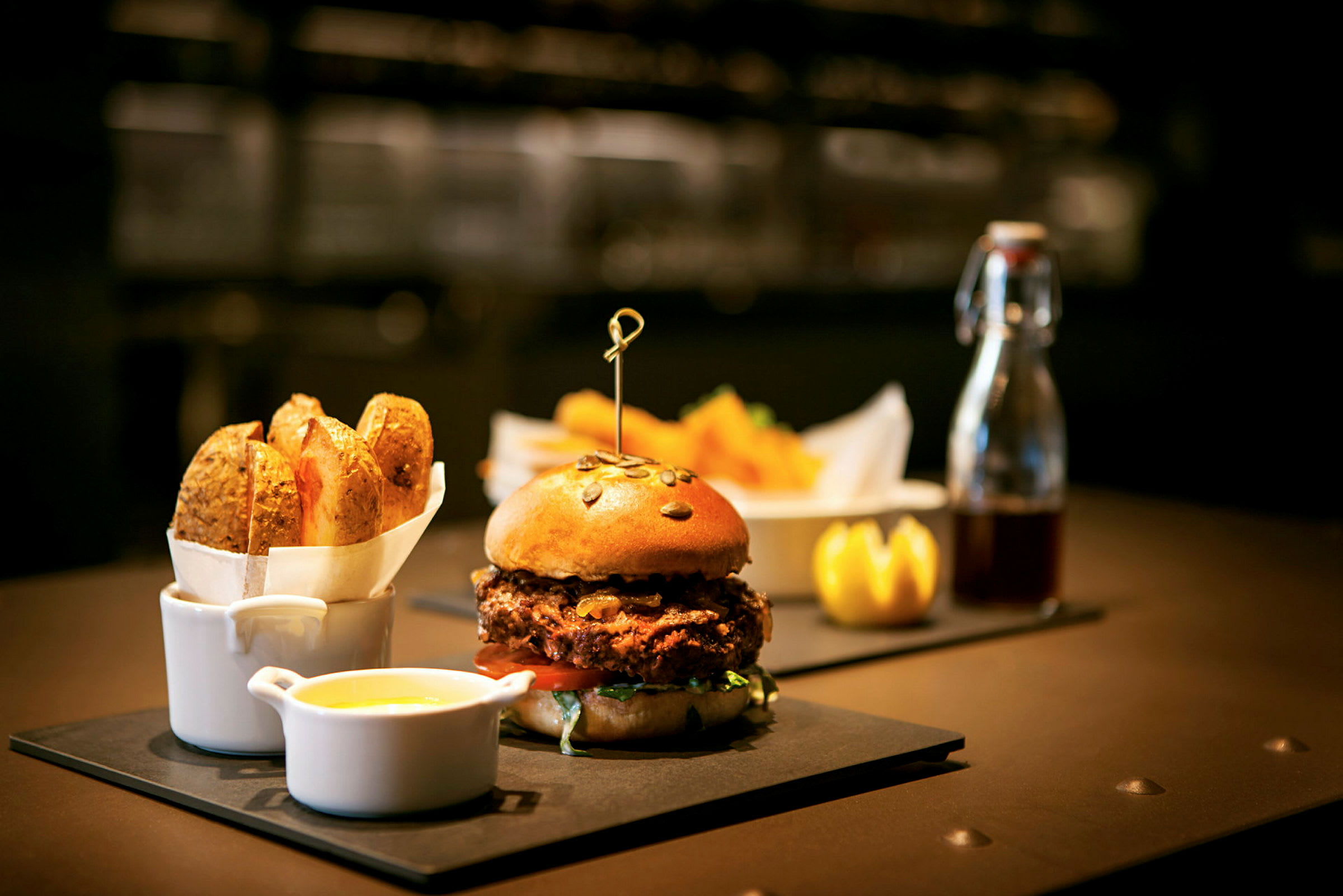 En burger med en bolle med frø serveres på en tallerken med en skål med sauce og pommes frites ved siden af. (AI-genereret tekst)