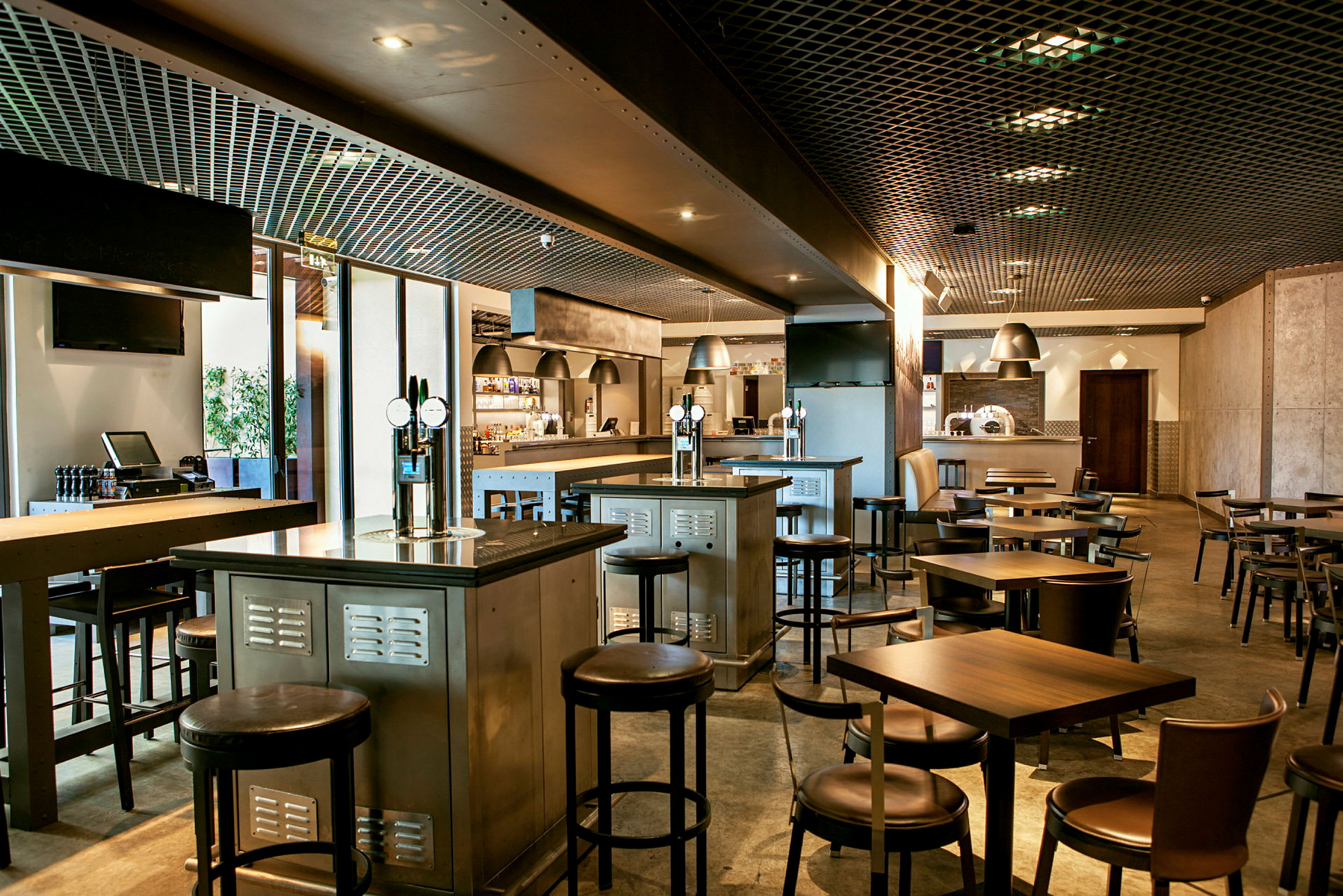 Et moderne restaurantinteriør med borde, stole og bardiske. Belysningen er dæmpet, og interiøret har en industriel stil. (AI-genereret tekst)