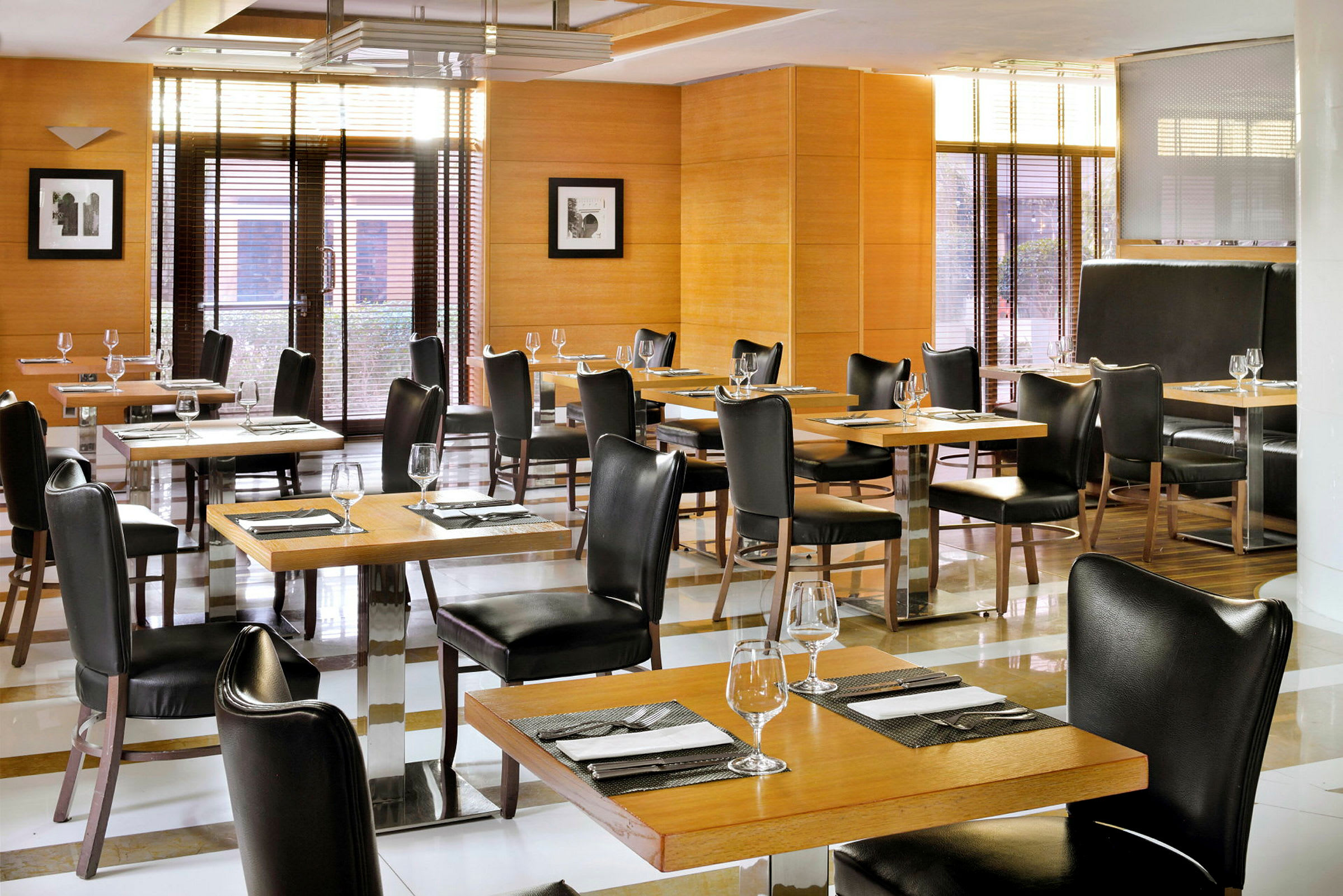 En restaurantsal med borde og stole i mørkt træ og læder, dækket med glas og servietter. (AI-genereret tekst)
