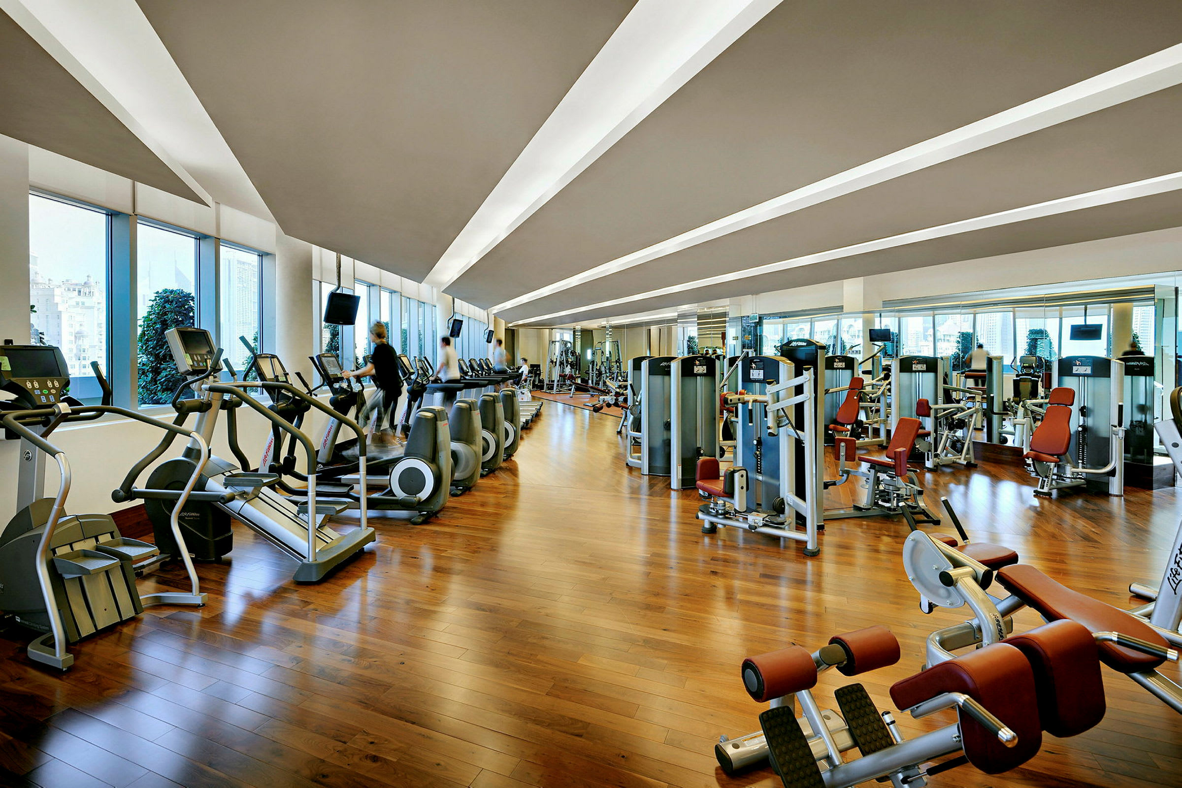 Billede af et fitnesscenter med træningsmaskiner og løbebånd ved store vinduer. (AI-genereret tekst)