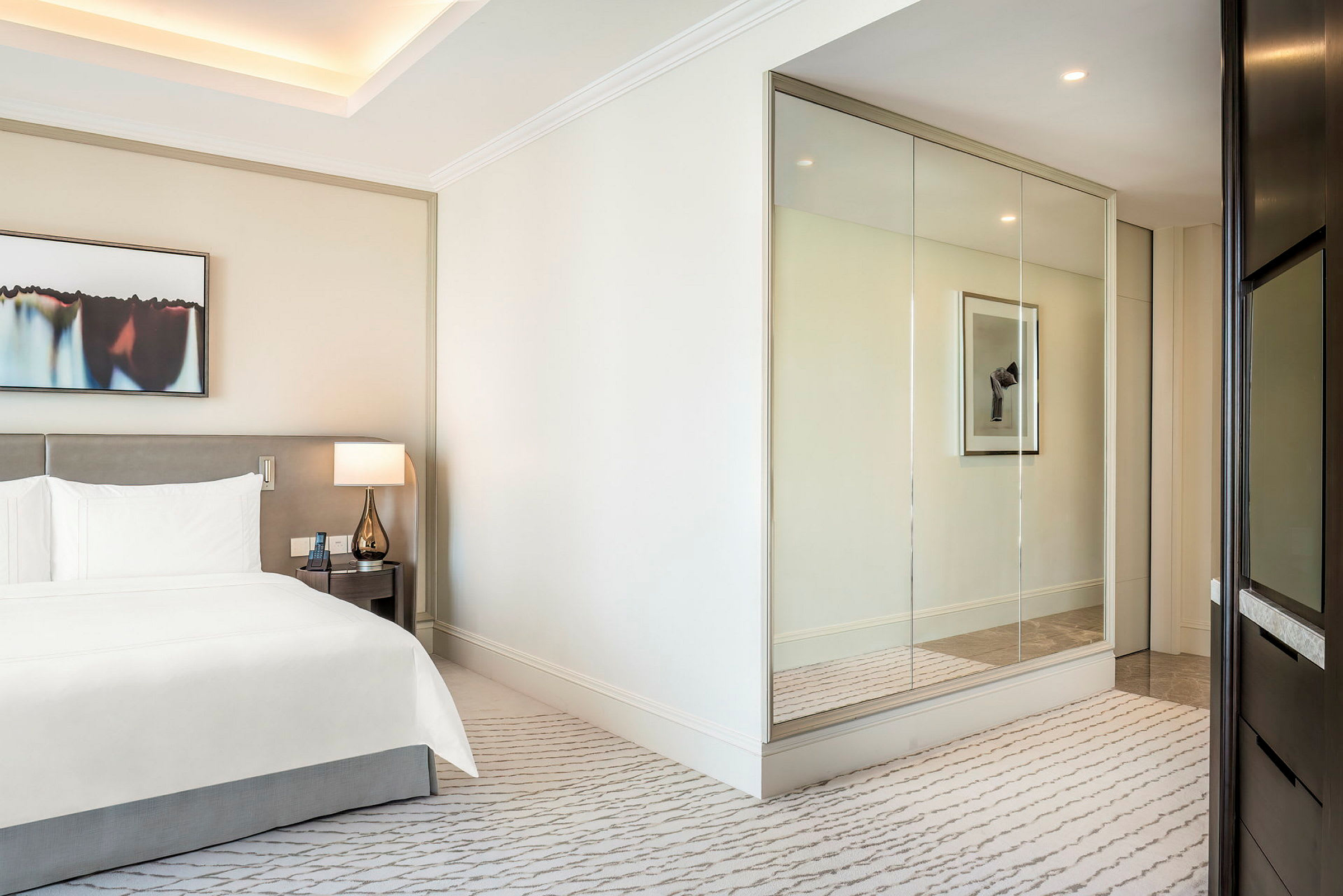 Et moderne og lyst hotelværelse med en dobbeltseng, en lampe på et natbord og en spejlvæg. (AI-genereret tekst)