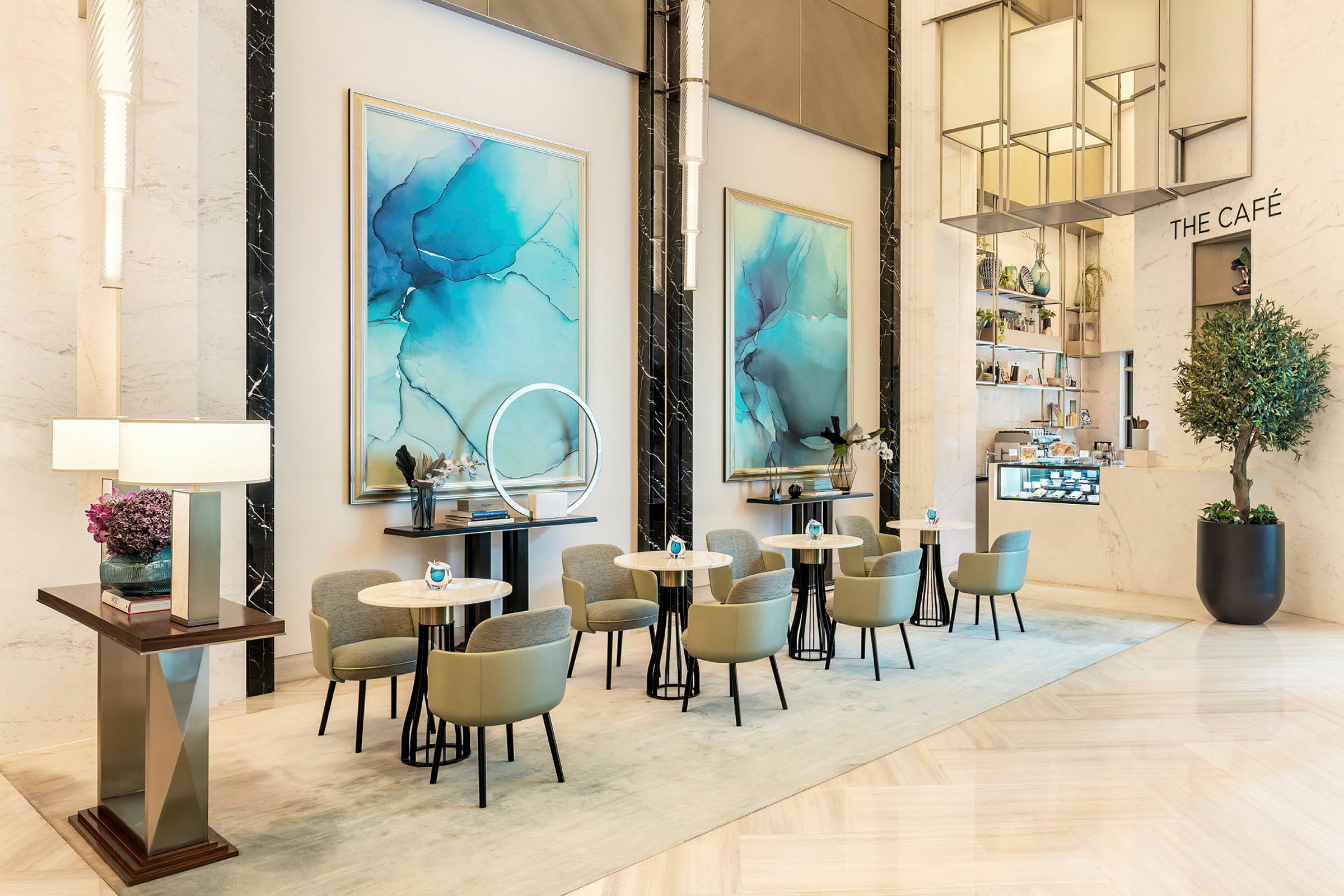 En moderne elegant café med små borde og stole i et lyst interiør, dekoreret med blåt abstrakt kunst på væggene. (AI-genereret tekst)