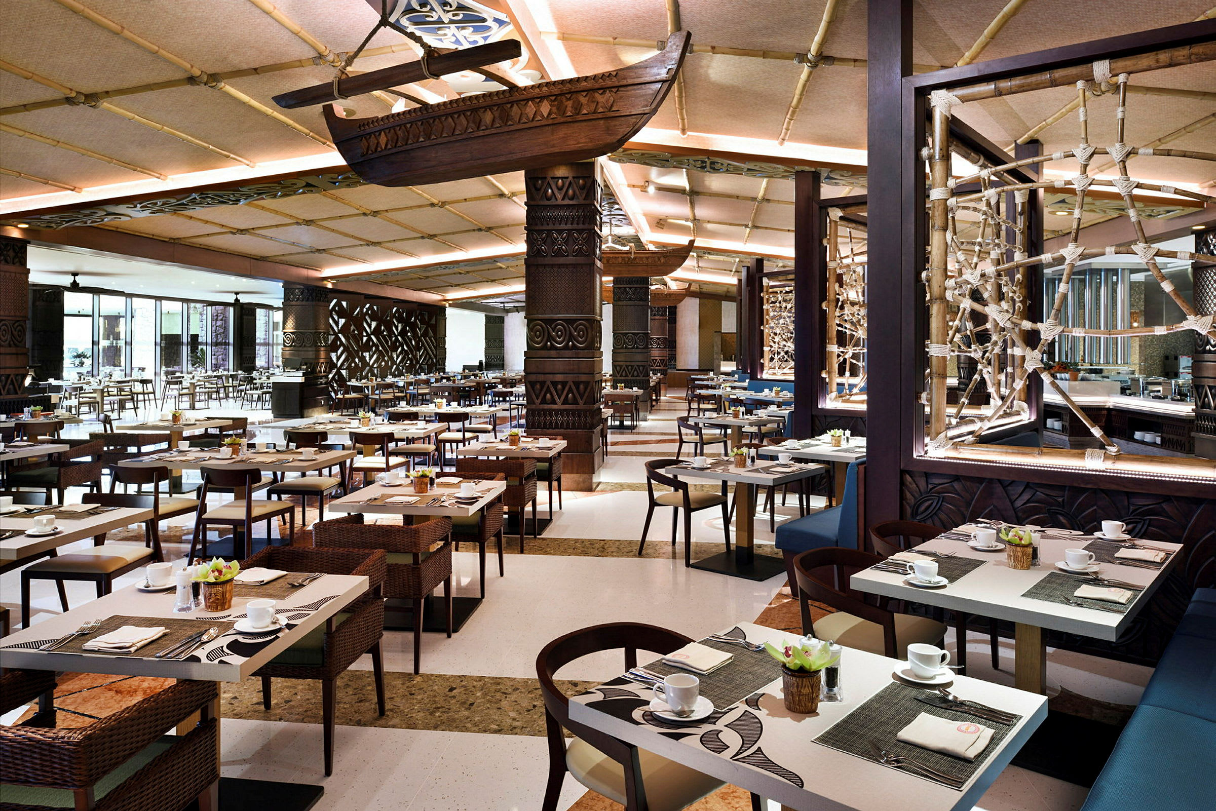 Indretning i en rummelig restaurant med borde dækket til måltider, dekorative lofter og vægge. Et skib hænger fra loftet som en del af dekorationen. (AI-genereret tekst)