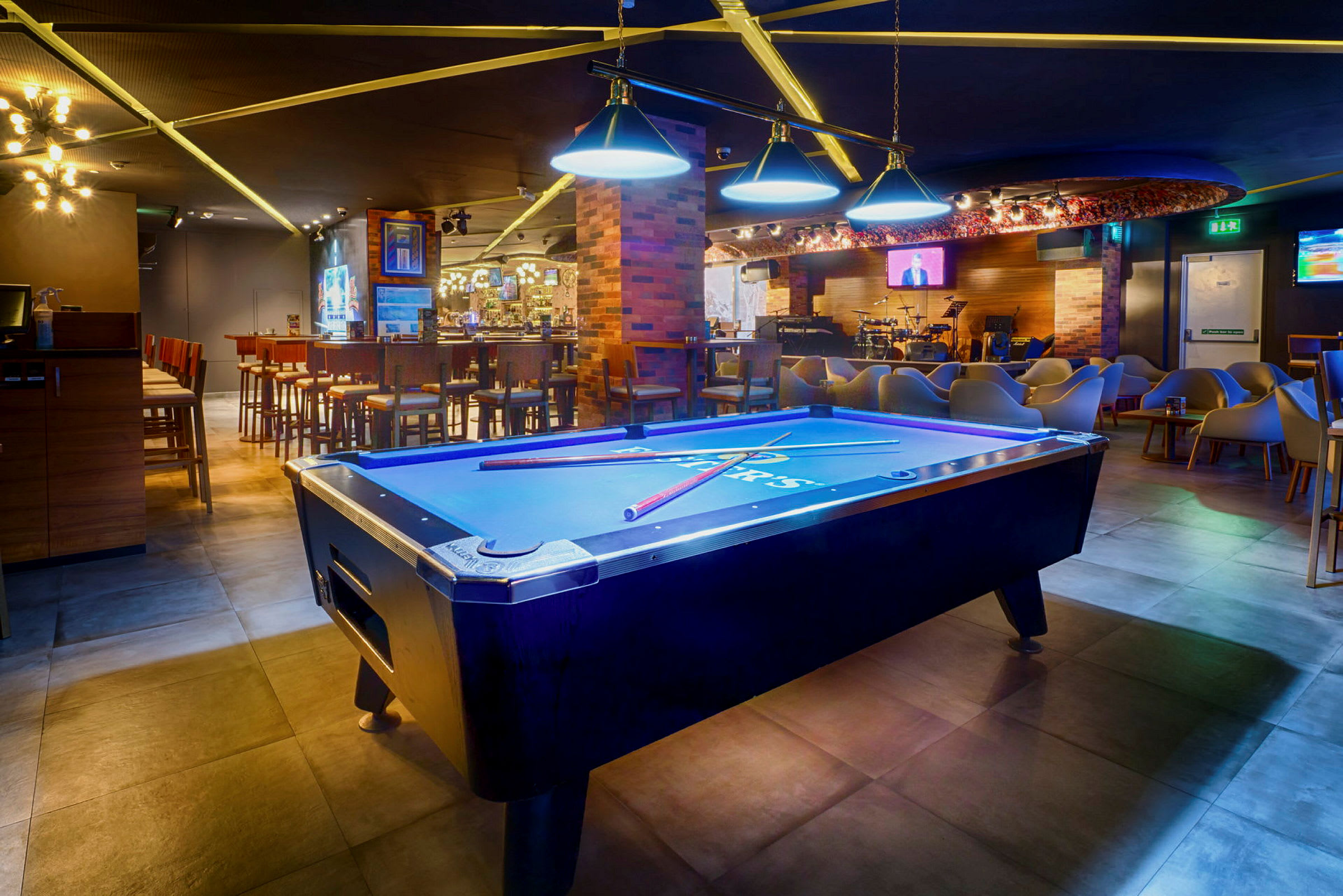 Billardbord i en farverigt oplyst lounge med bar og siddepladser. (AI-genereret tekst)