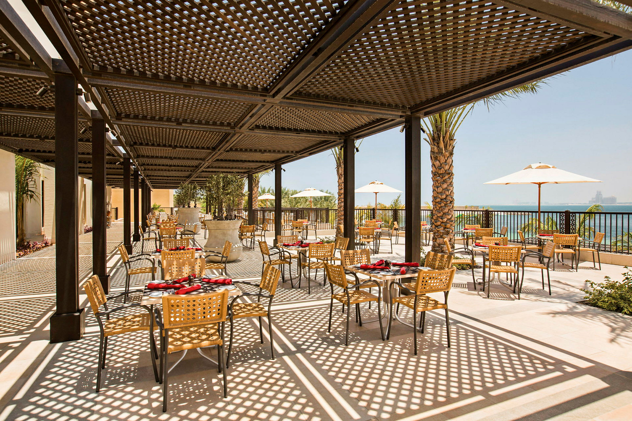 Udendørs restaurant med borde og stole under skyggefuld pergola. (AI-genereret tekst)
