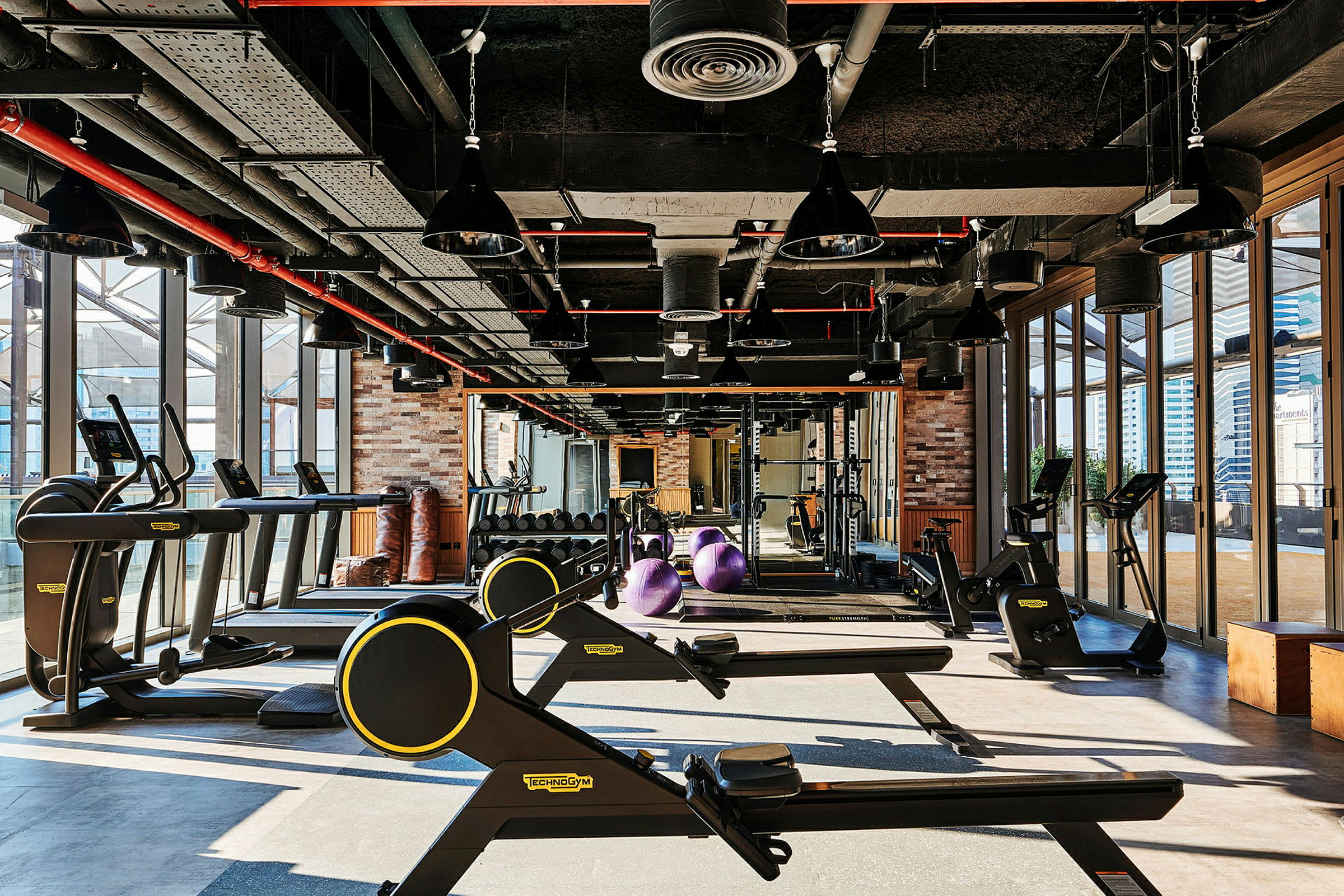 Billede af et fitnesscenter med træningsudstyr som løbebånd, romaskiner og håndvægte, samt store vinduer. (AI-genereret tekst)