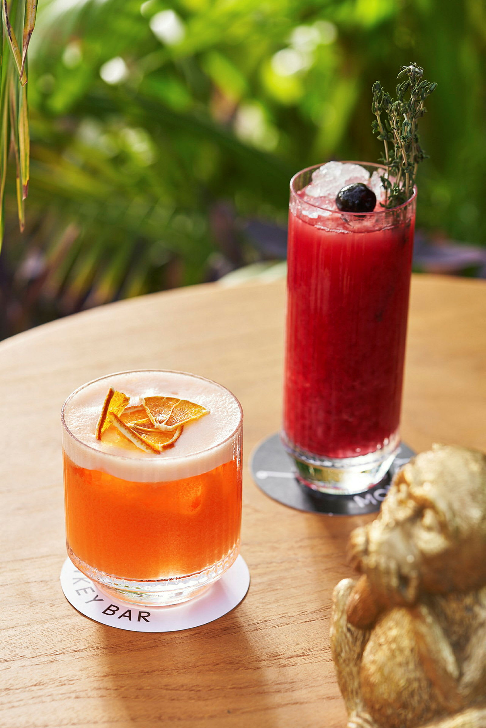 To drinks, en orange med skum og en mørkerød med is, står på et bord. (AI-genereret tekst)