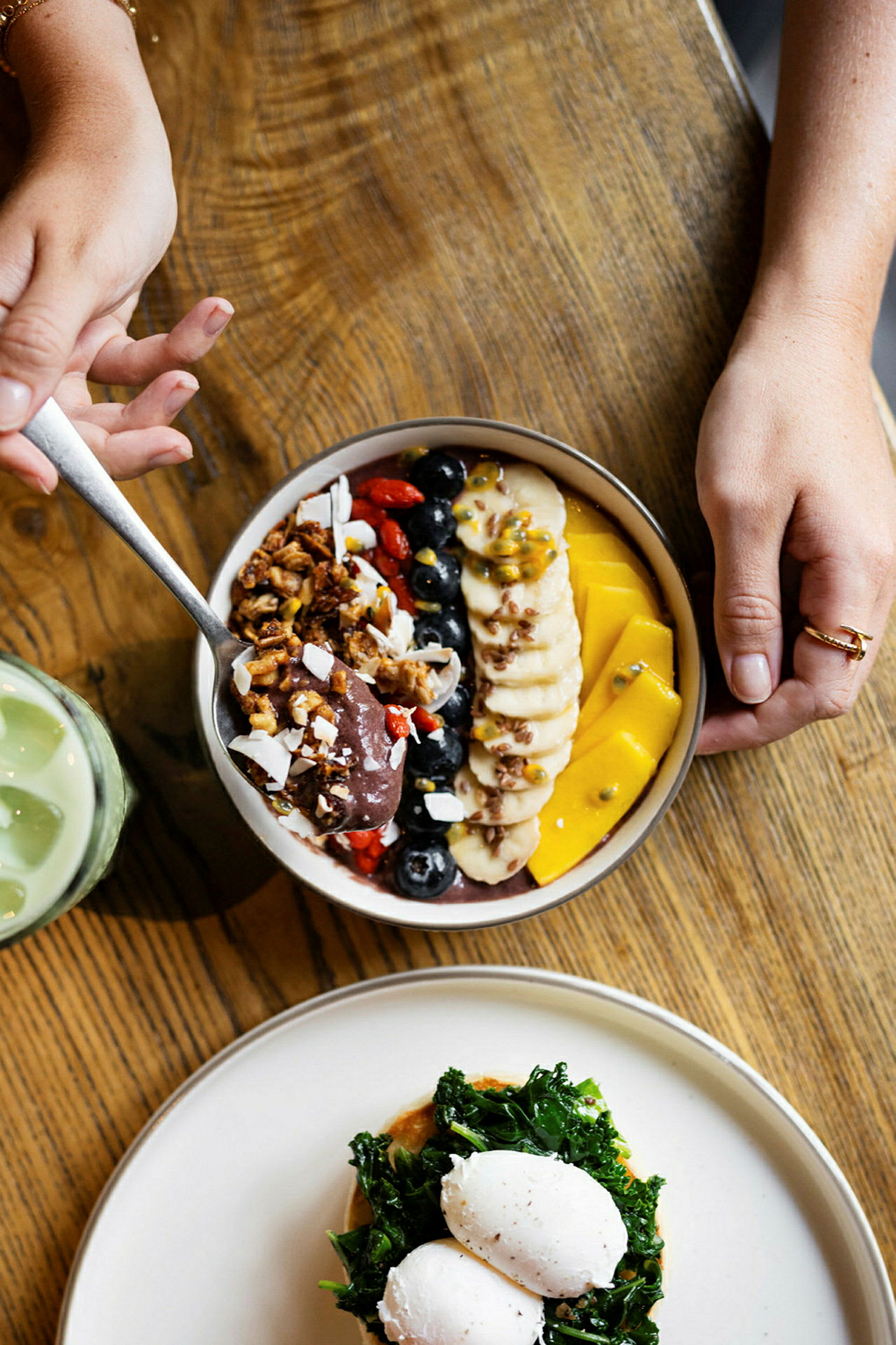 En tallerken med en farverig acai-bowl og en anden med pocherede æg og grøntsager på et træbord. (AI-genereret tekst)