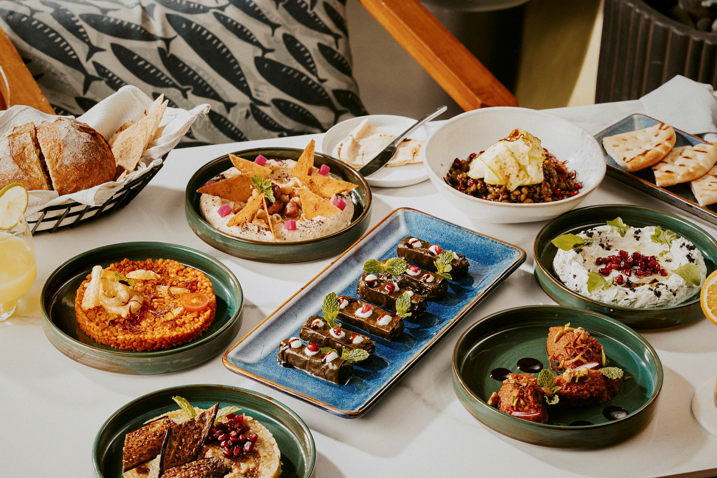 Et bord med forskellige retter, herunder brød, hummus, salat og dolma, serveret på tallerkener. (AI-genereret tekst)
