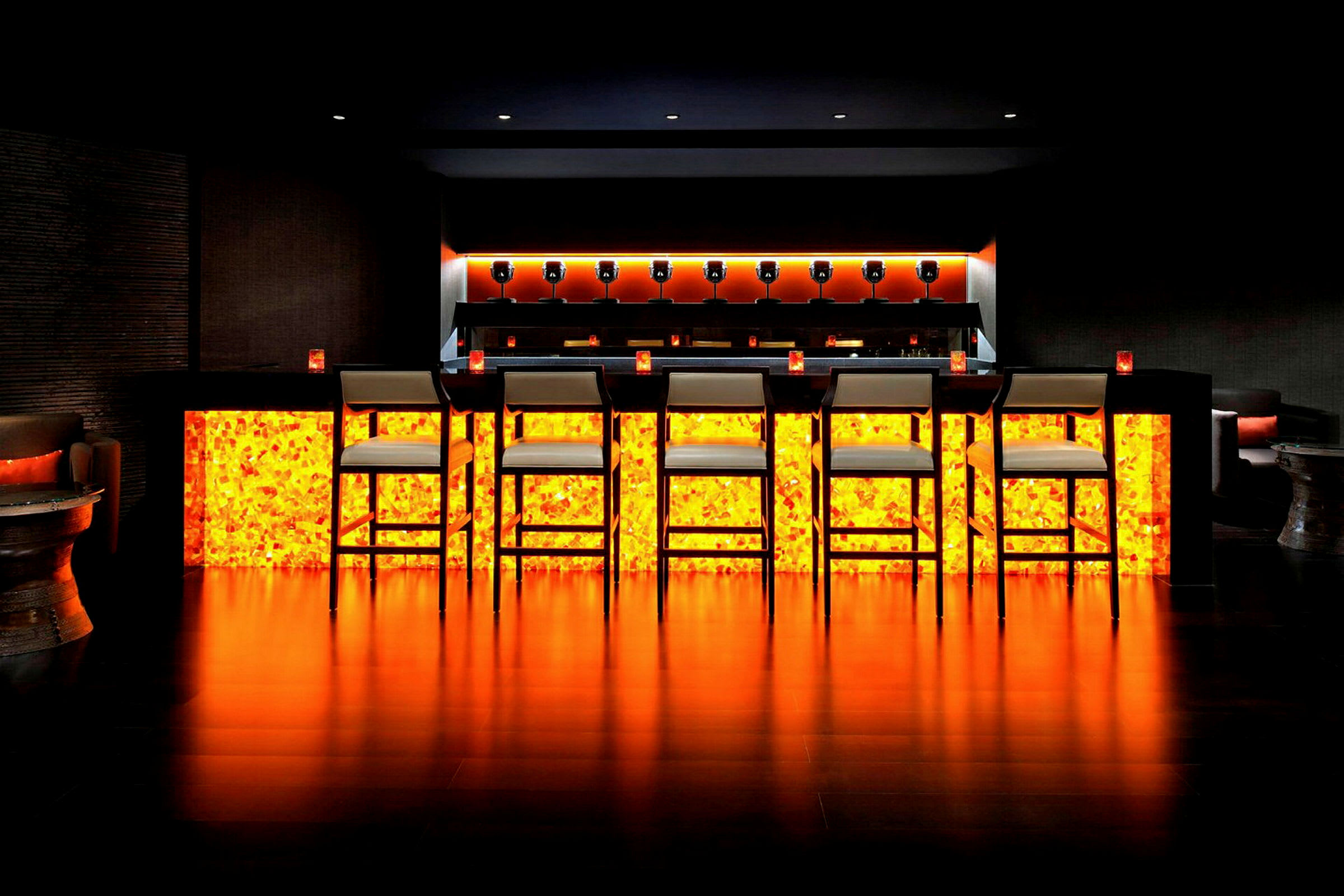 En bar med oplyst orange underside, høje stole og en moderne indretning. (AI-genereret tekst)
