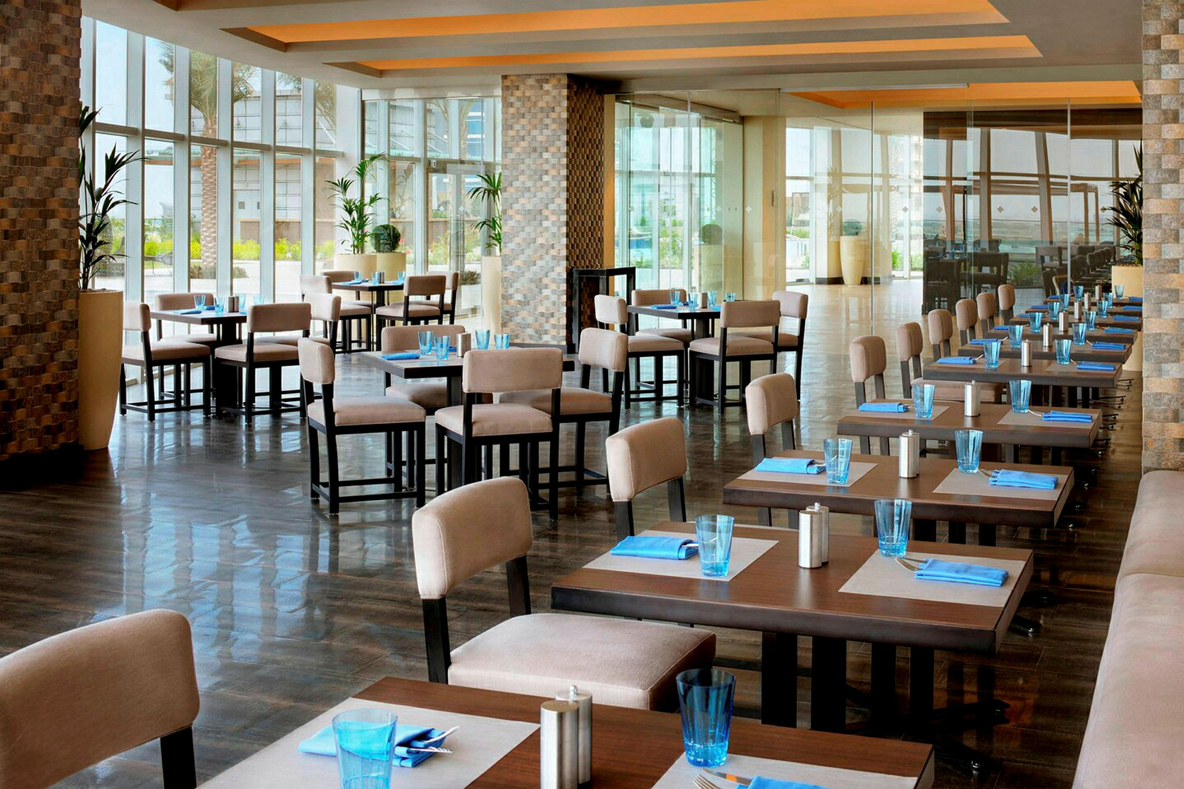 En åben restaurant med opdækkede borde, lyse stole og store vinduer. (AI-genereret tekst)