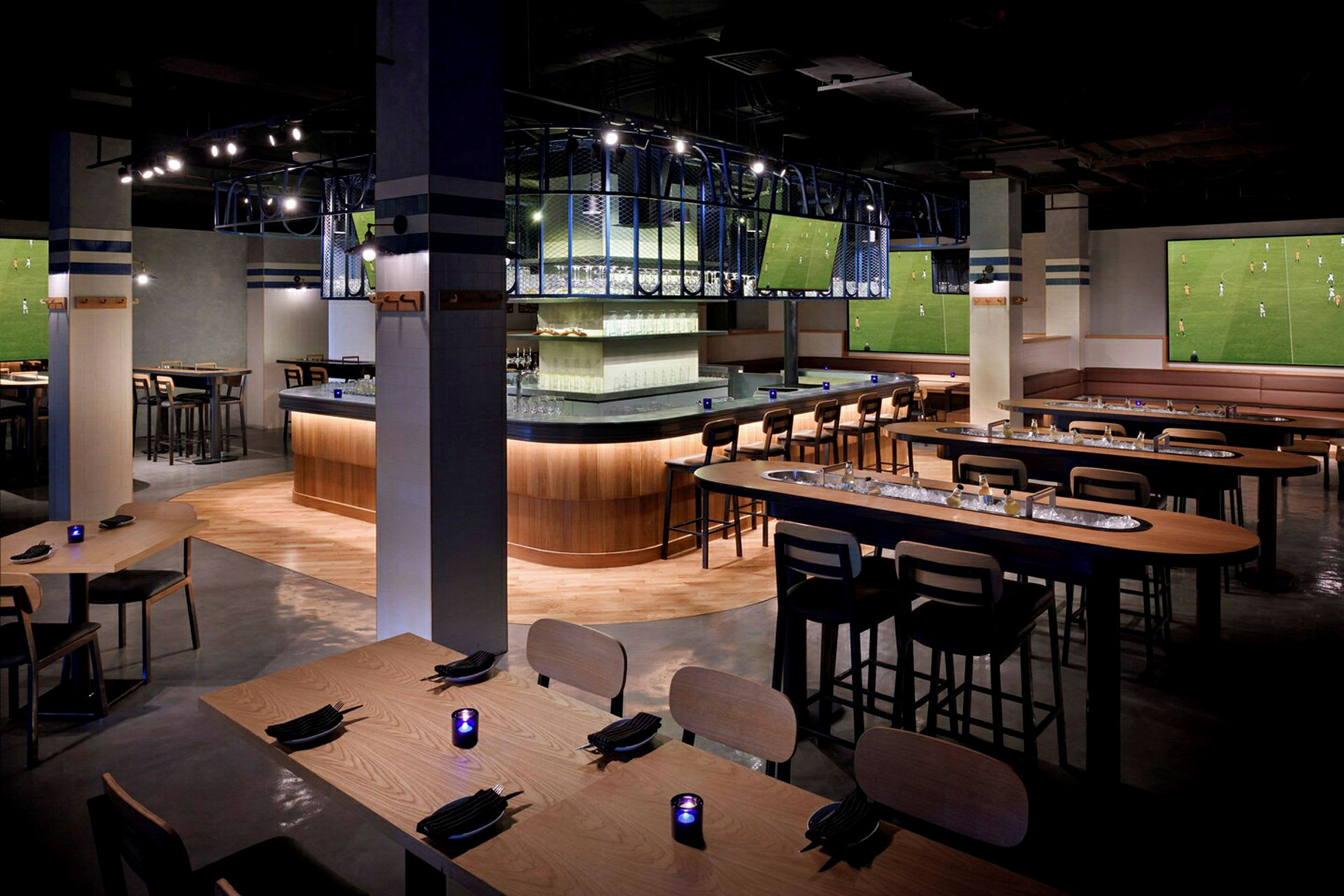 Interiør af en moderne bar med siddegrupper, flere borde og stole samt store skærme på væggene. (AI-genereret tekst)