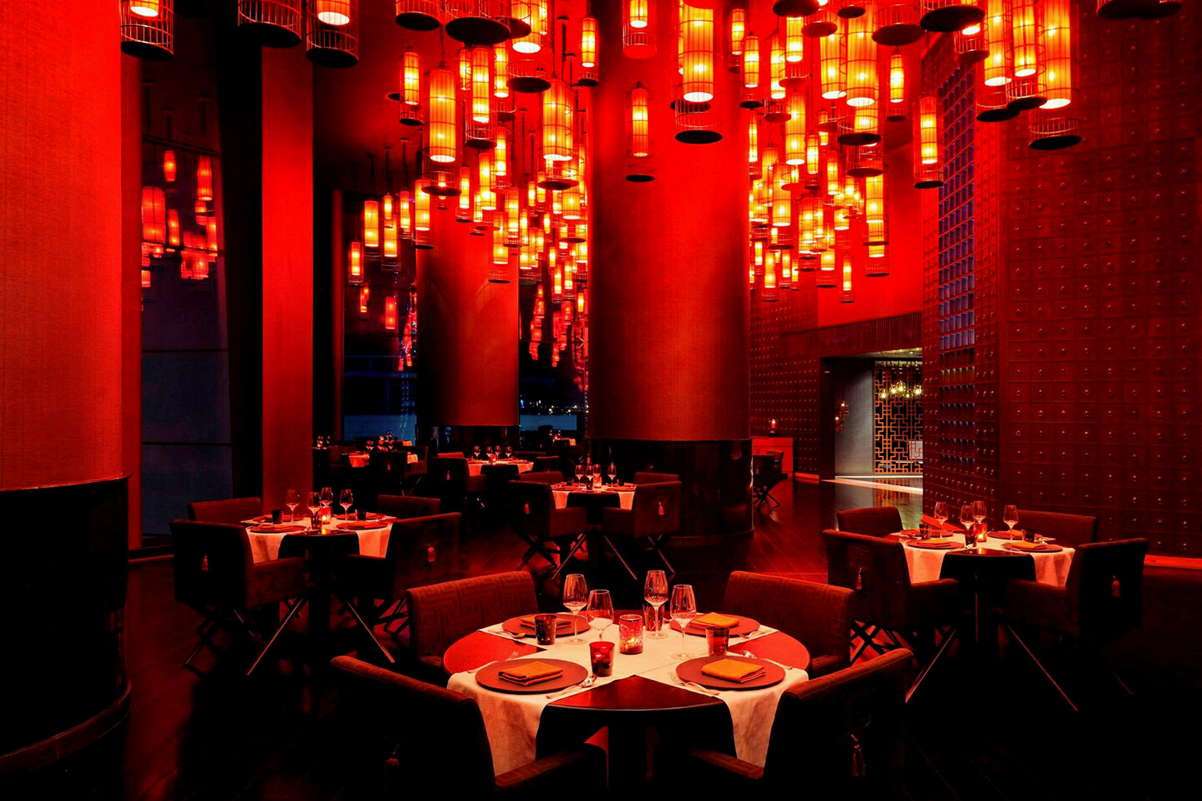 En restaurant med borde dækket til middag og mange røde lamper hængende fra loftet. (AI-genereret tekst)