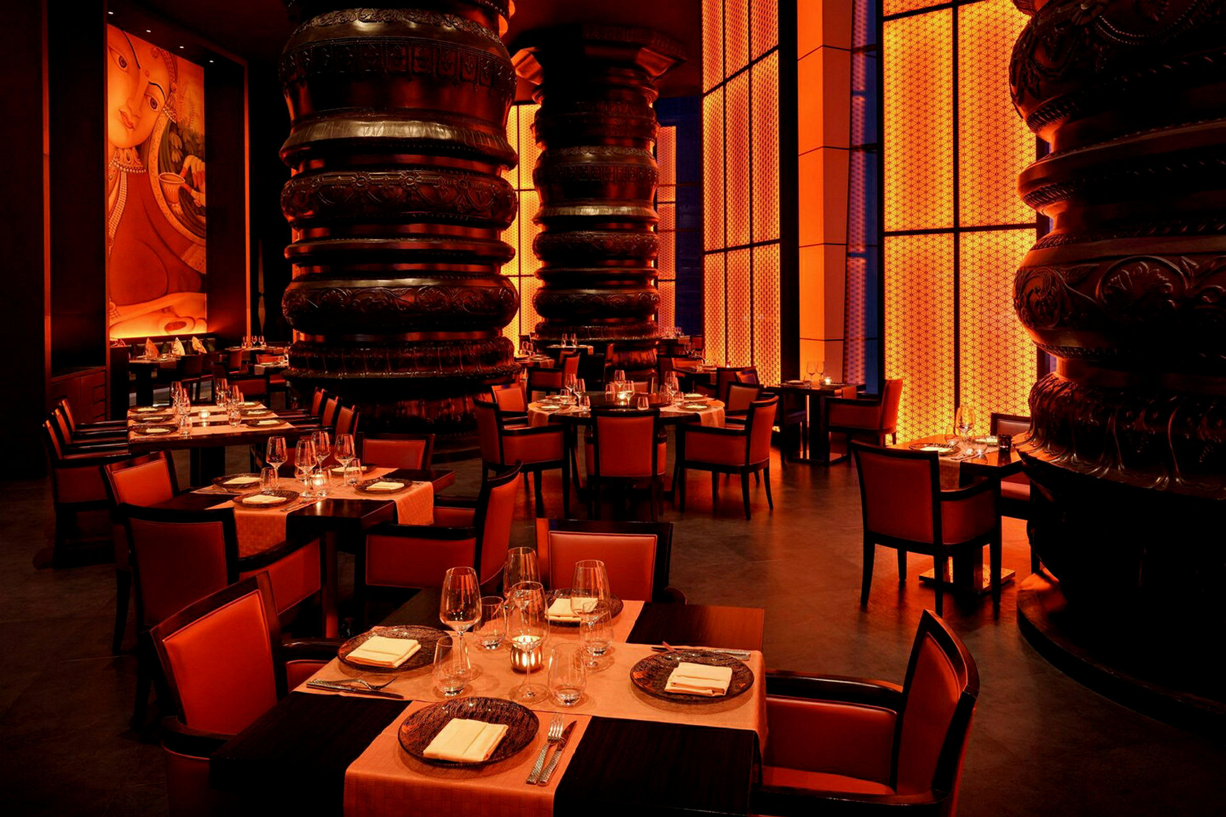 Interiør af en elegant restaurant med orange belysning, udsmykkede søjler og dækkede borde. (AI-genereret tekst)