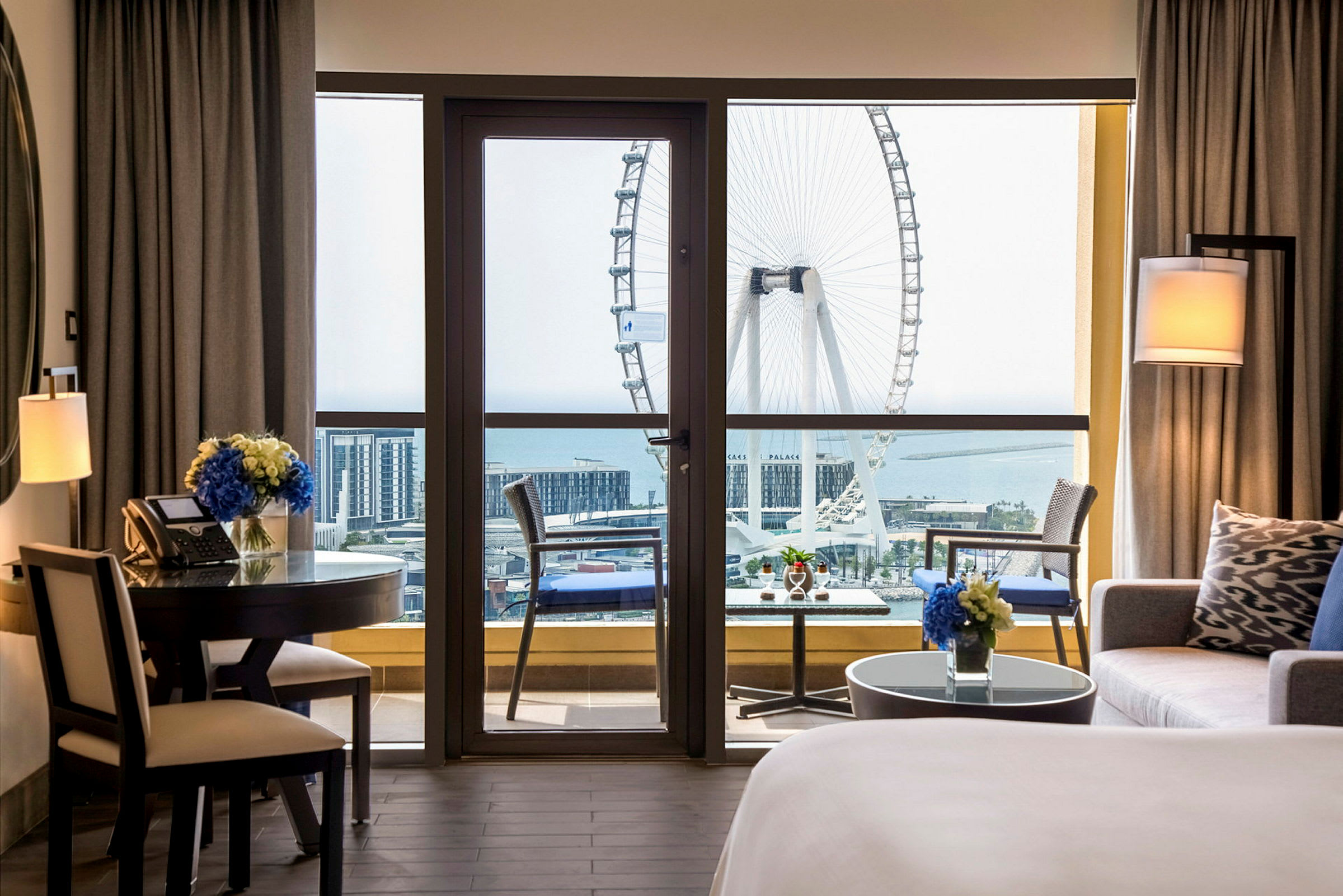 Et hotelværelse med en balkon, der har udsigt over et stort pariserhjul og havet. (AI-genereret tekst)