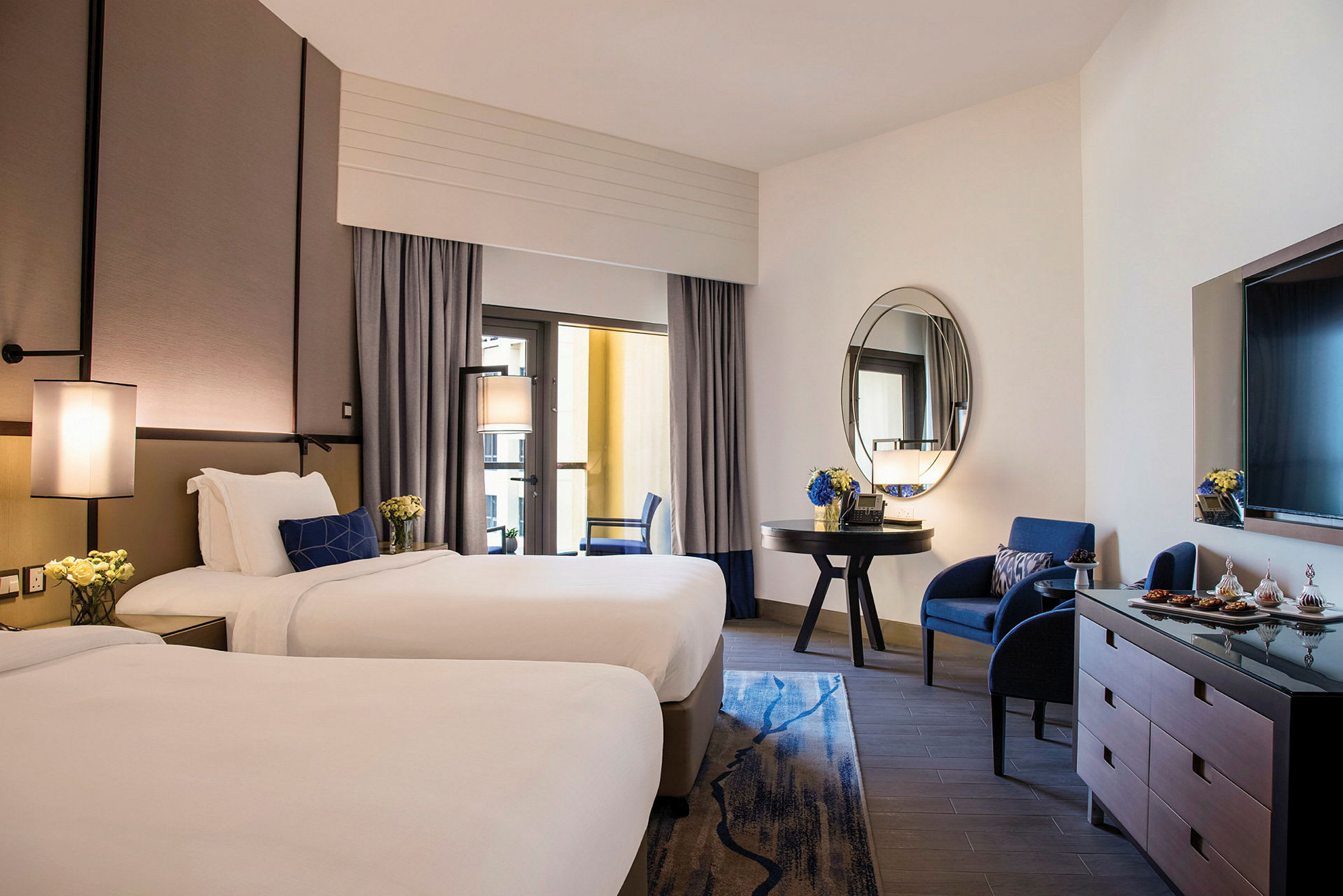 Hotelværelse med to enkeltsenge, en siddegruppe og et spejl. (AI-genereret tekst)